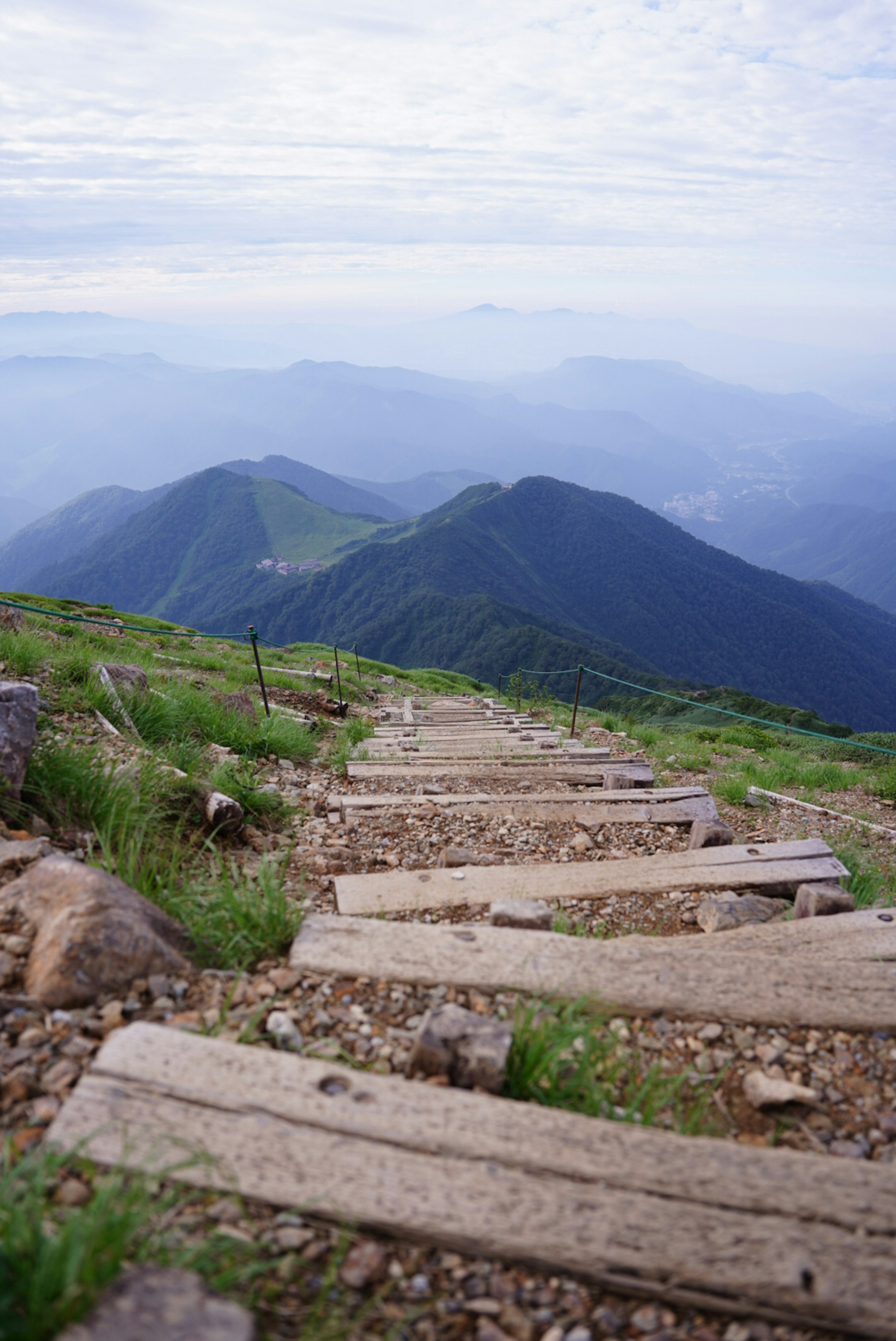 山道の木製階段と緑の草原が広がる風景