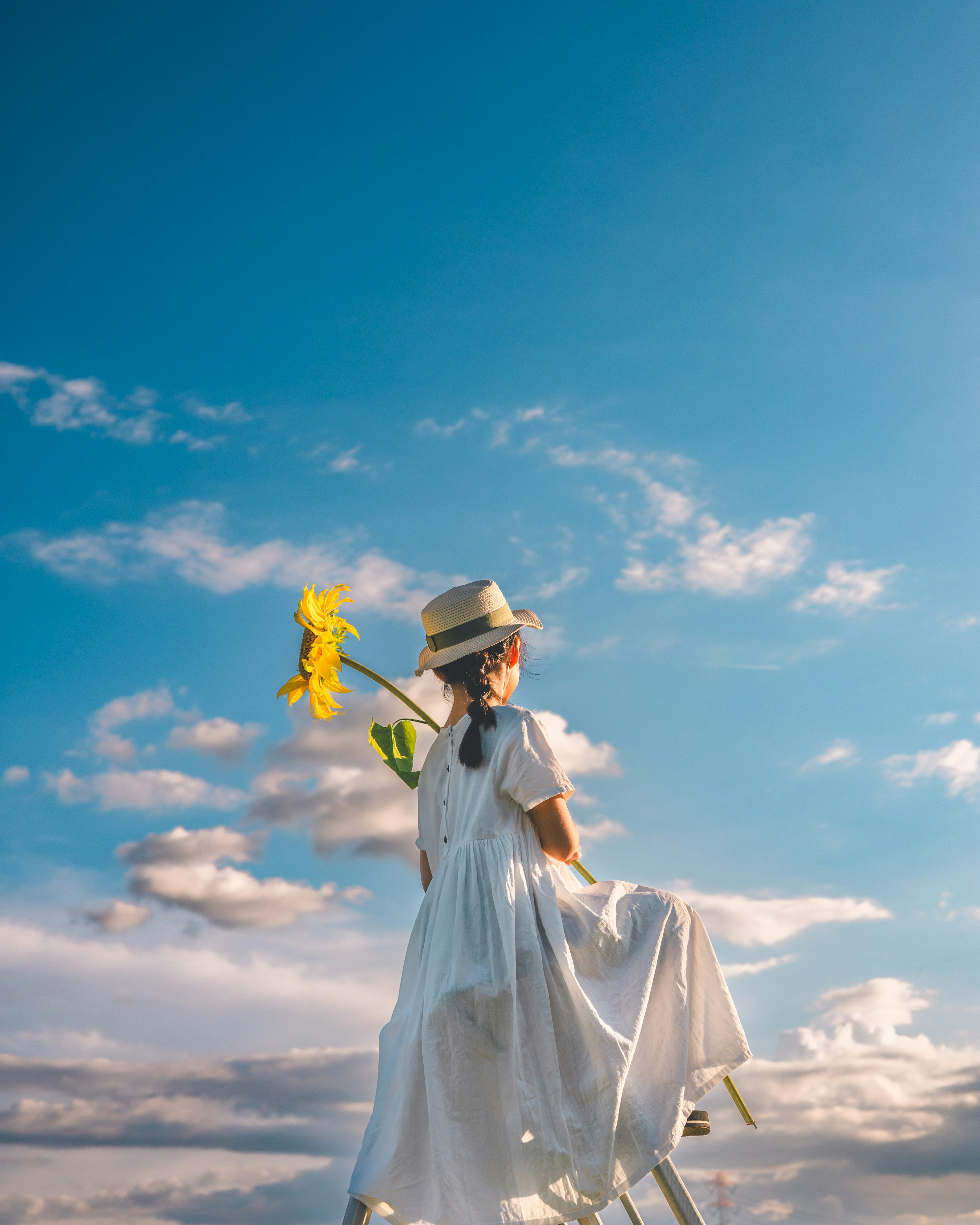 青空の下で花を持つ白いドレスの少女