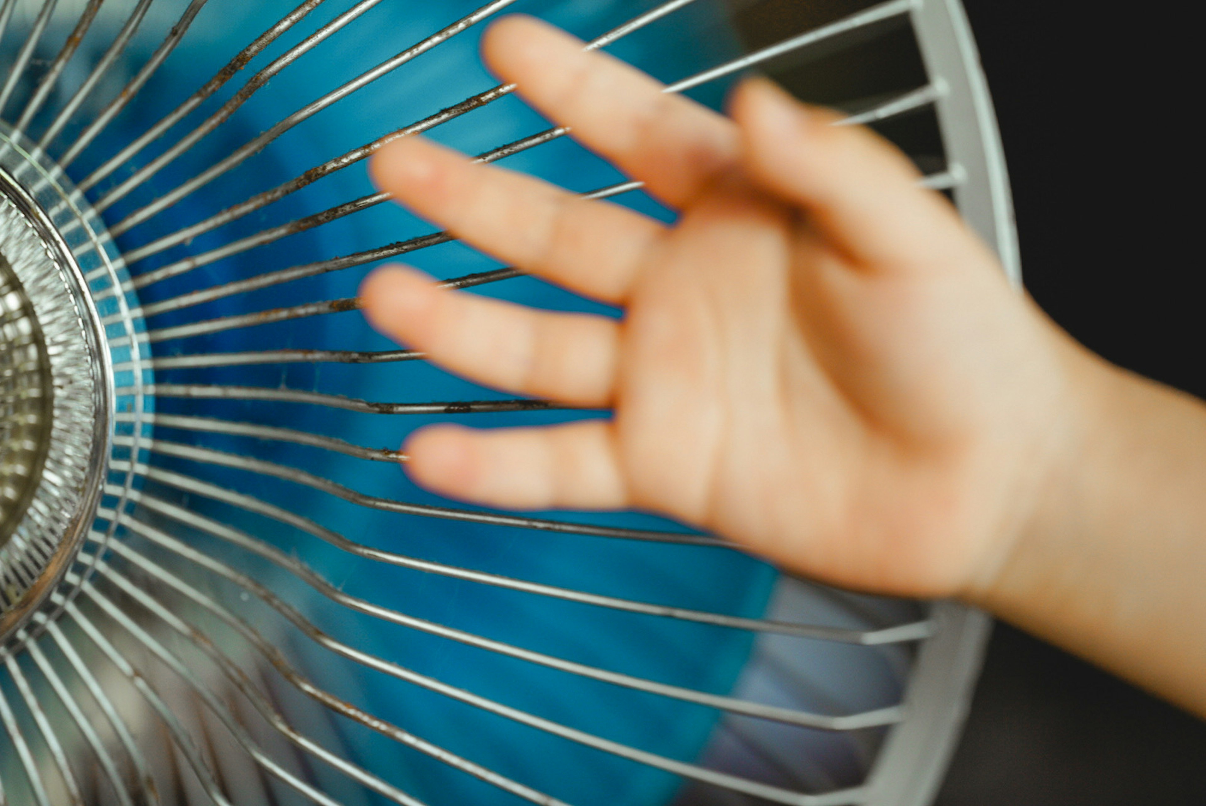 Hand in der Nähe eines Ventilators mit blauem Hintergrund und metallischem Design