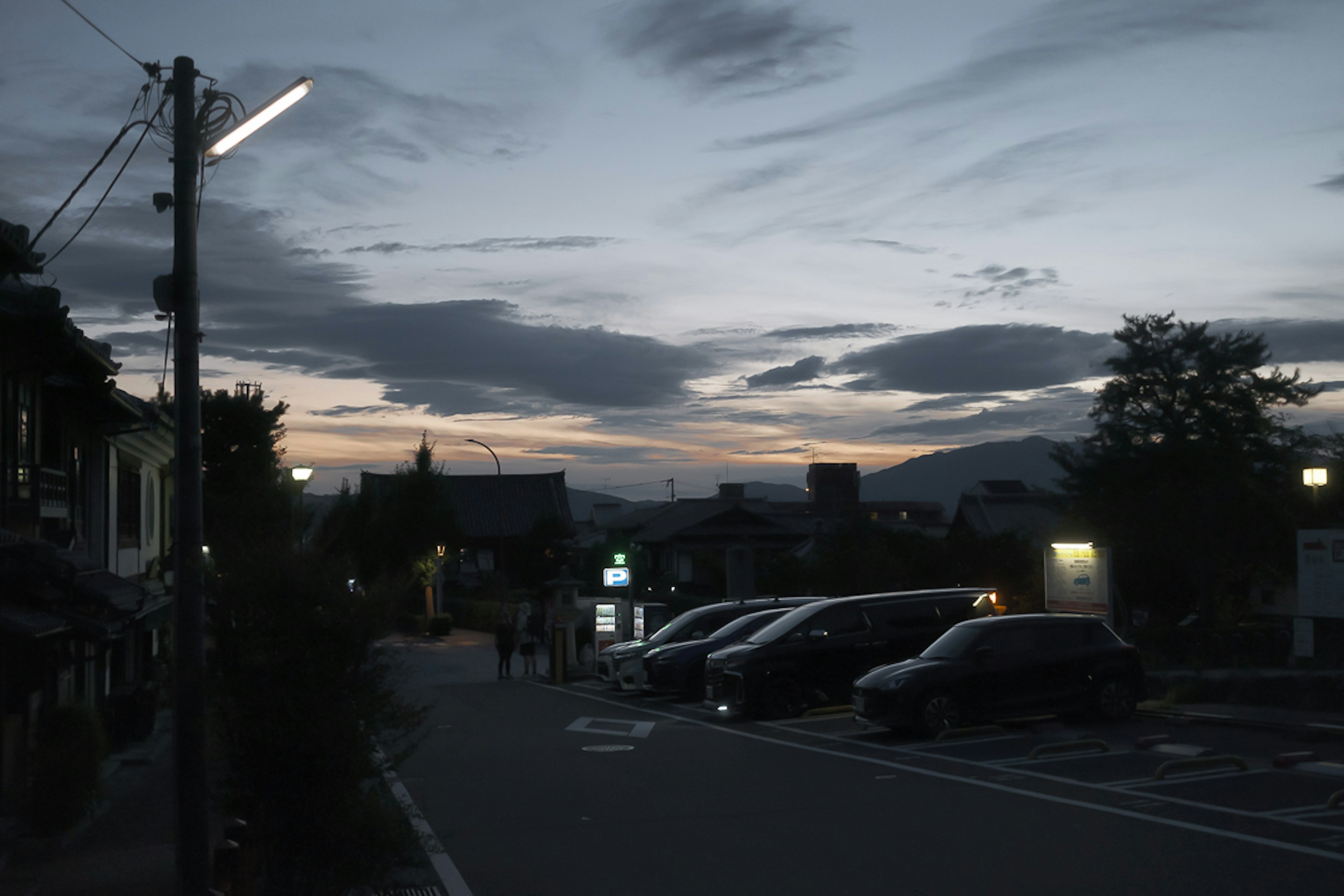 Quiet street scene at dusk with parked cars and cloudy sky