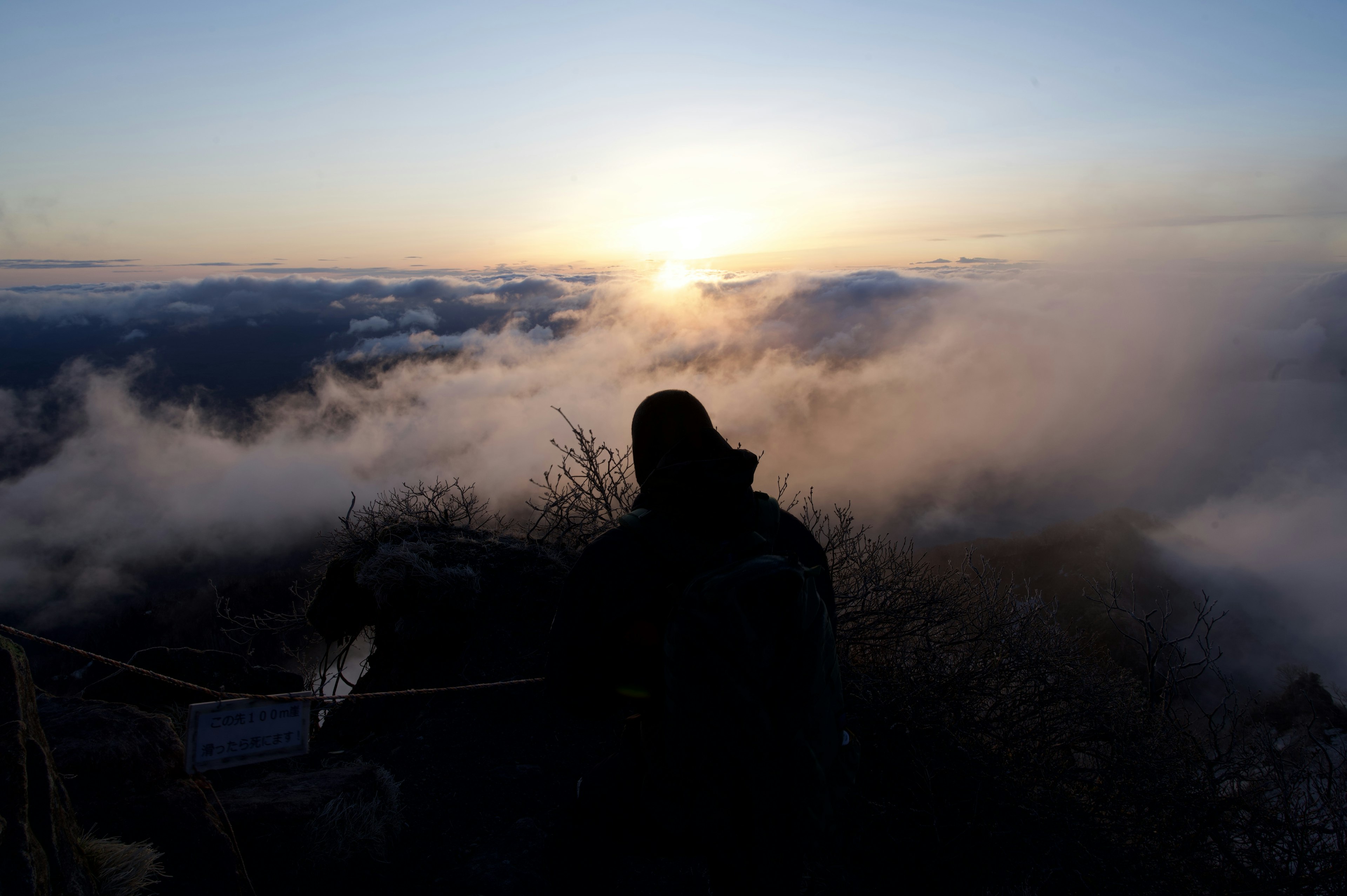 Siluet seseorang di puncak gunung dengan matahari terbit yang indah di atas awan