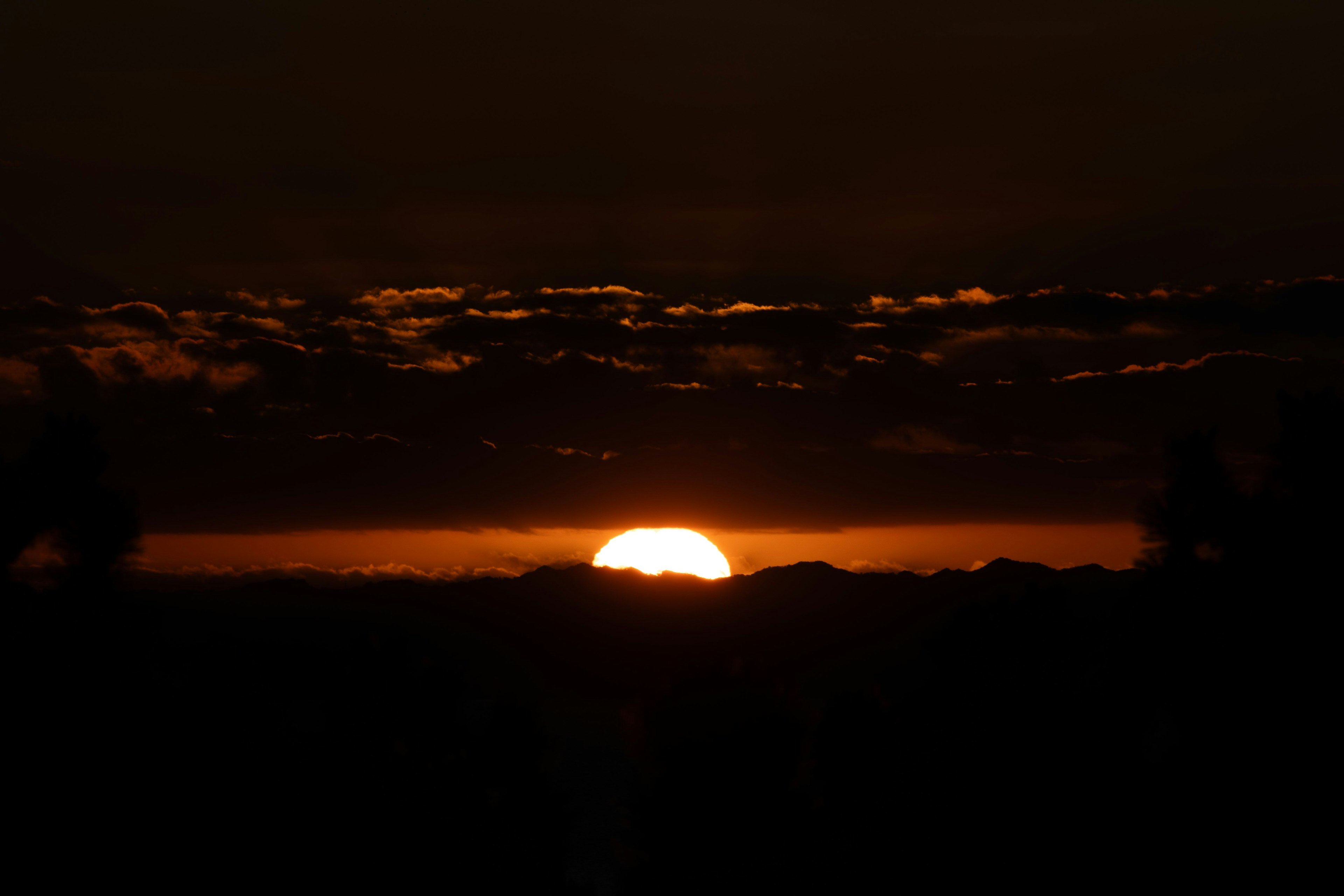 夕日が山の向こうに沈む美しい風景 暗い空にオレンジ色の光が広がる