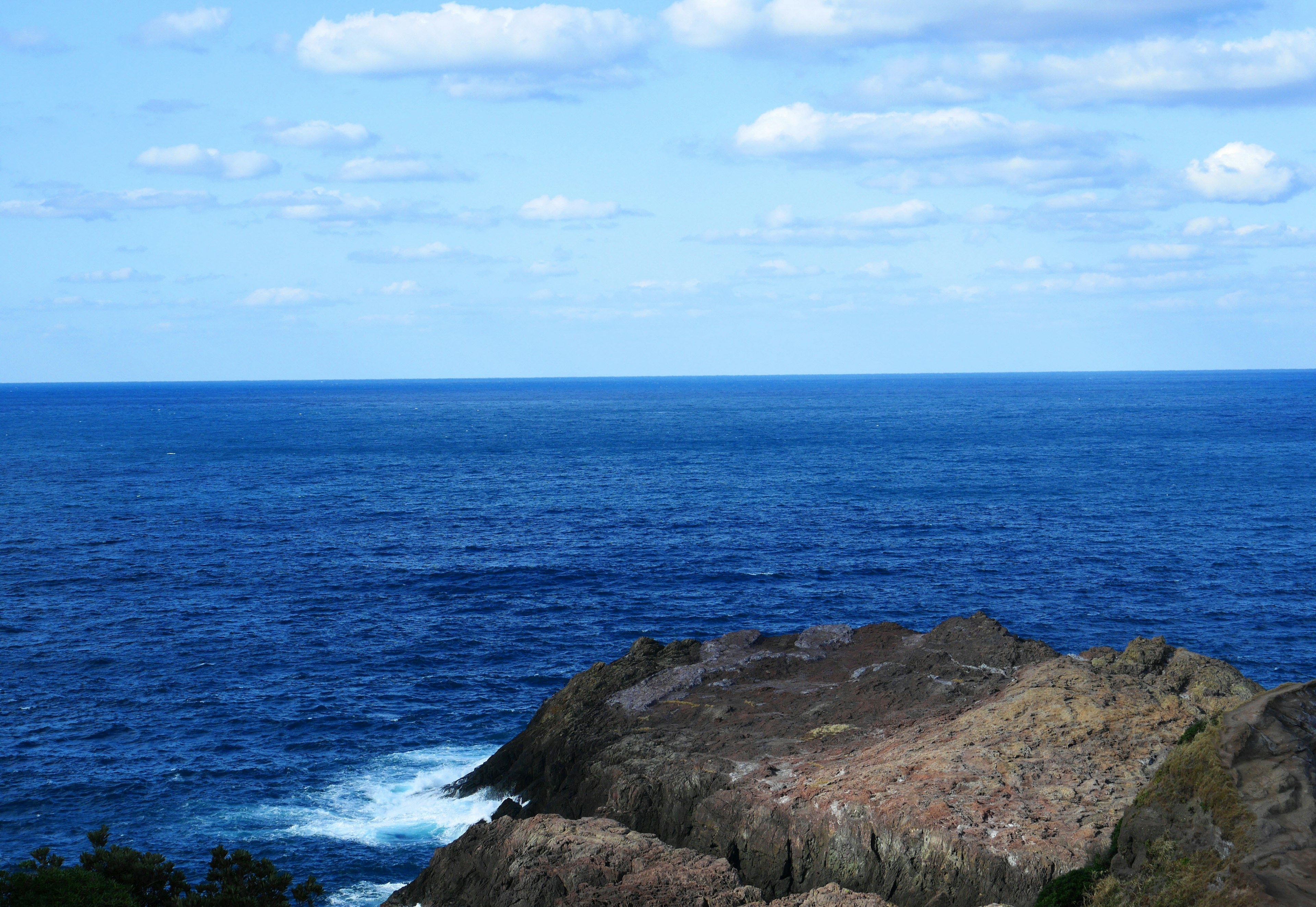 Scenic view of blue ocean and sky with clouds featuring a rocky foreground