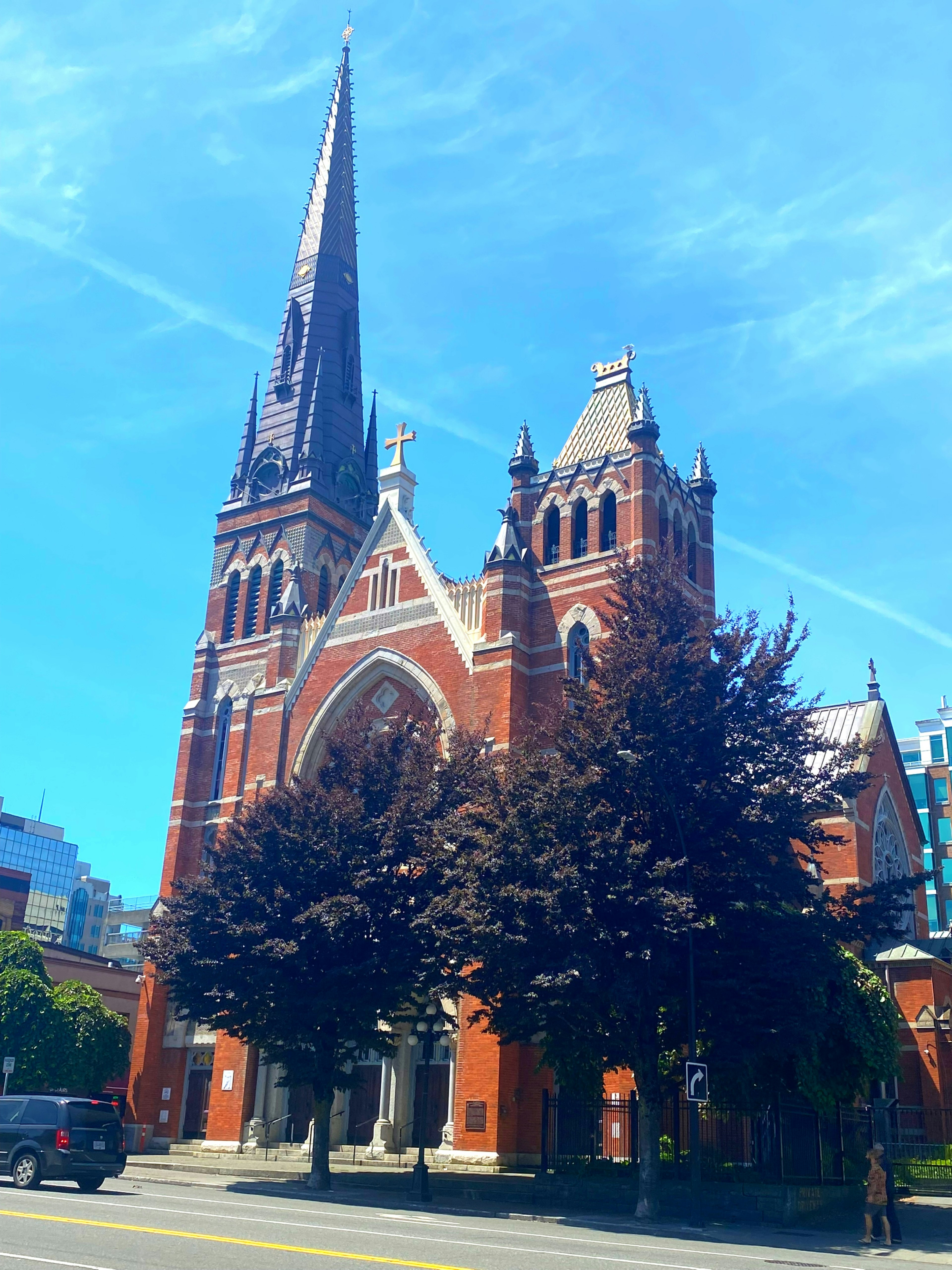 Église en briques rouges avec une haute flèche et des arbres environnants