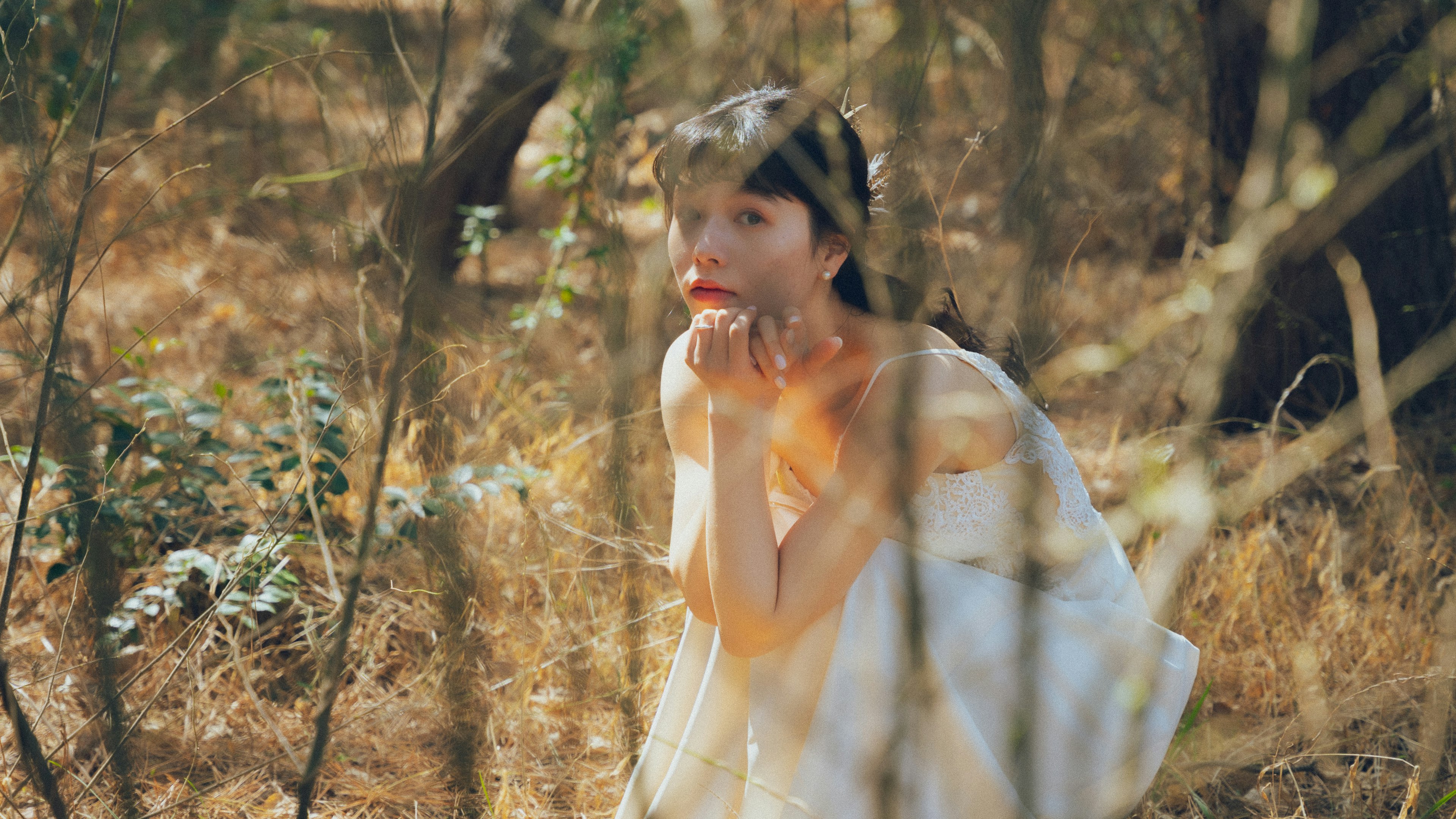 Una mujer con un vestido blanco visible entre los árboles en un bosque