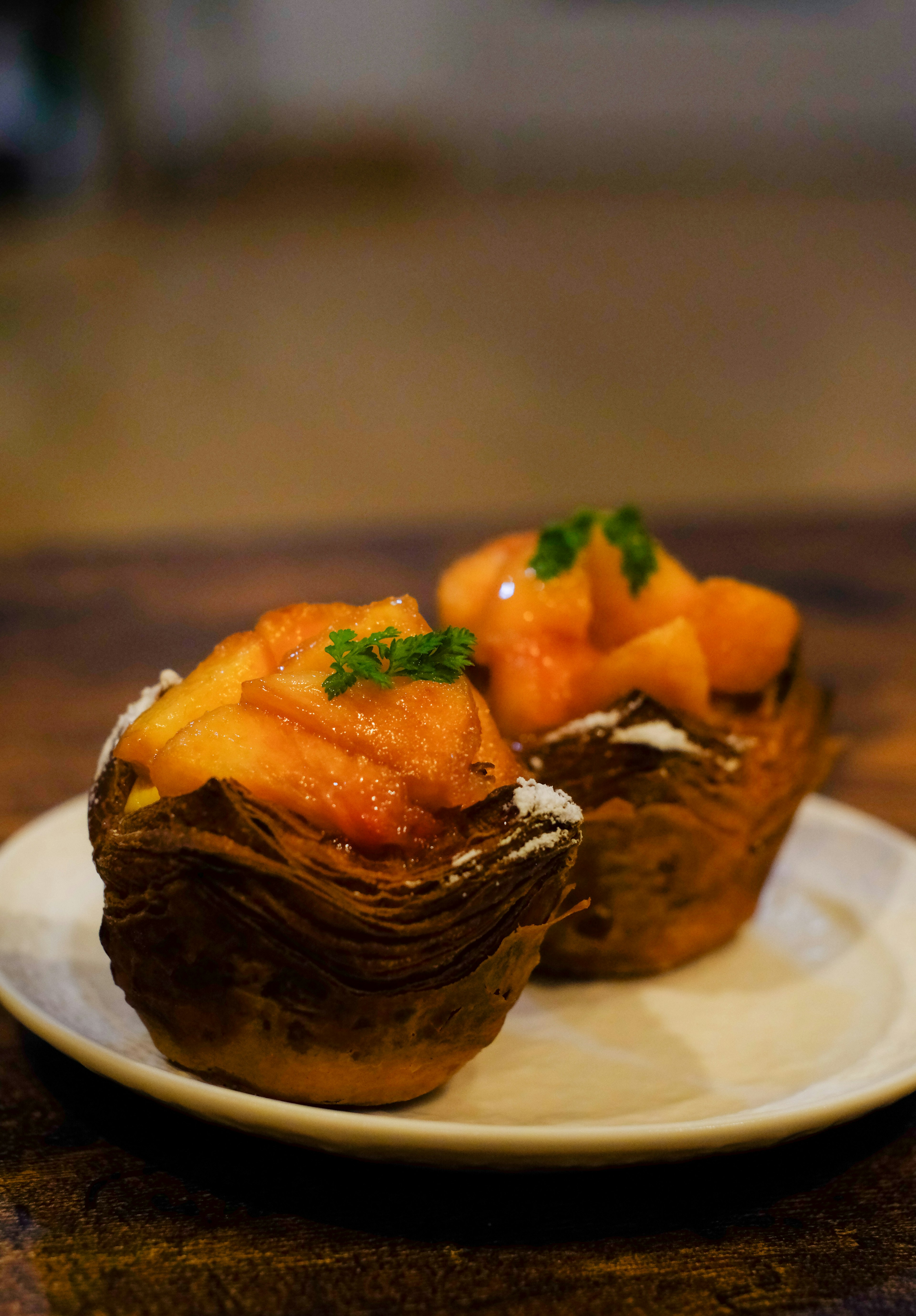 Dos postres de masa hojaldrada cubiertos con frutas naranjas y hierbas verdes en un plato blanco