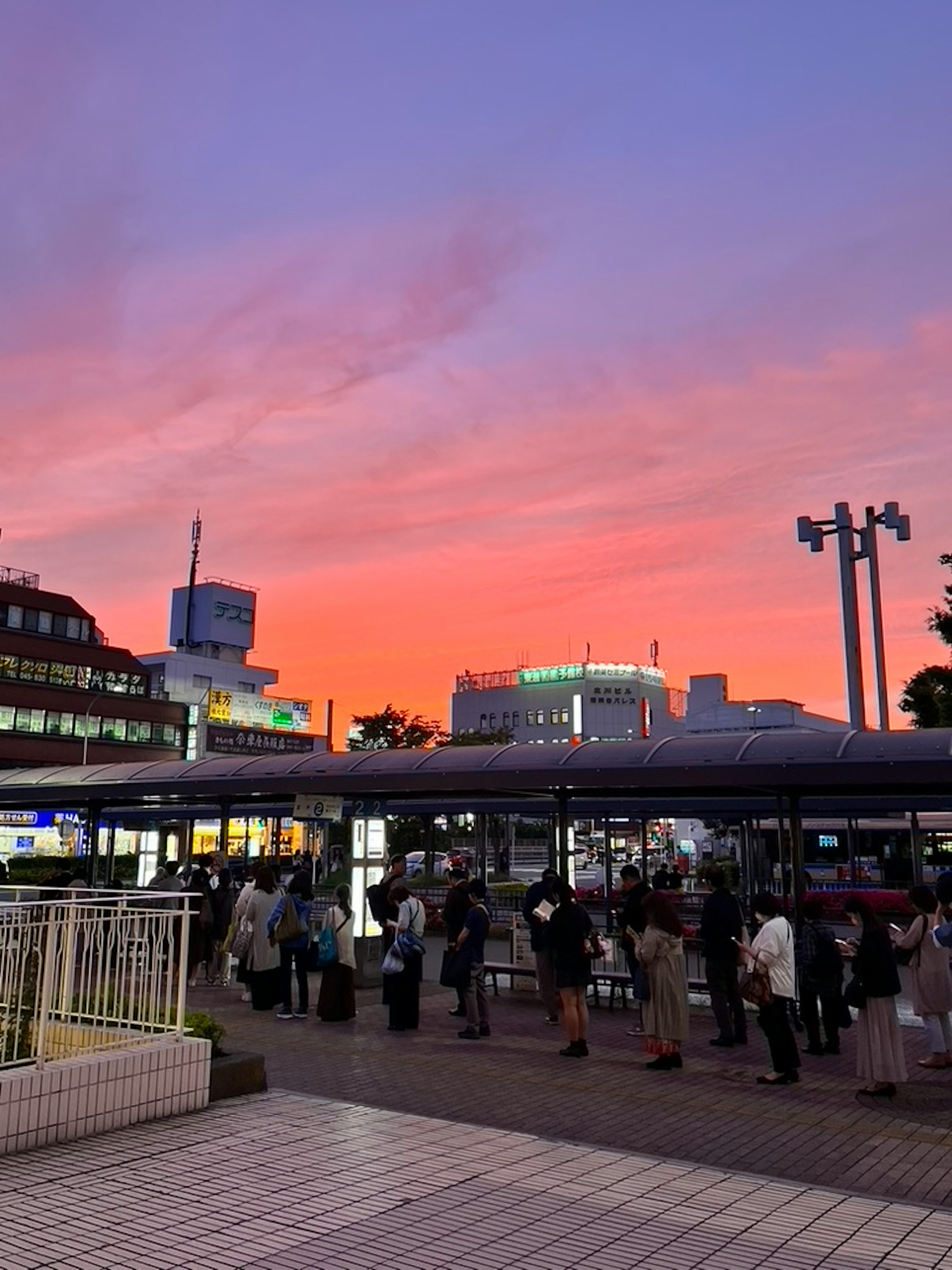 夕焼けの空を背景に並ぶ人々と駅の風景