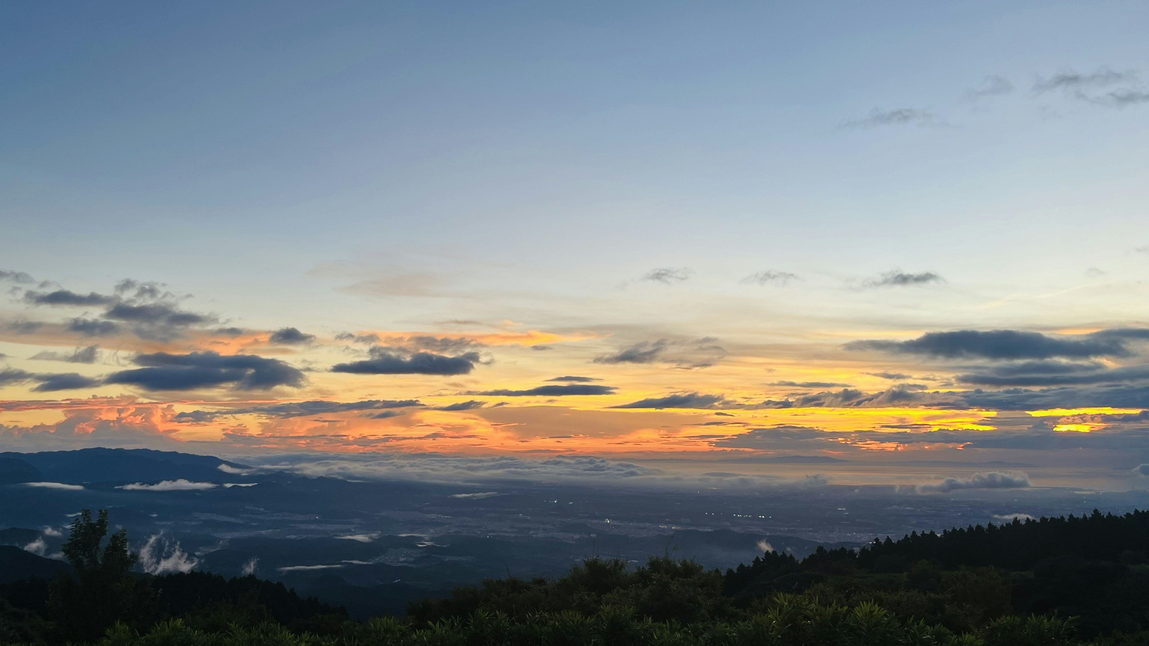 美しい夕焼けの風景、青空にオレンジと黄色の雲、山々と谷が広がる