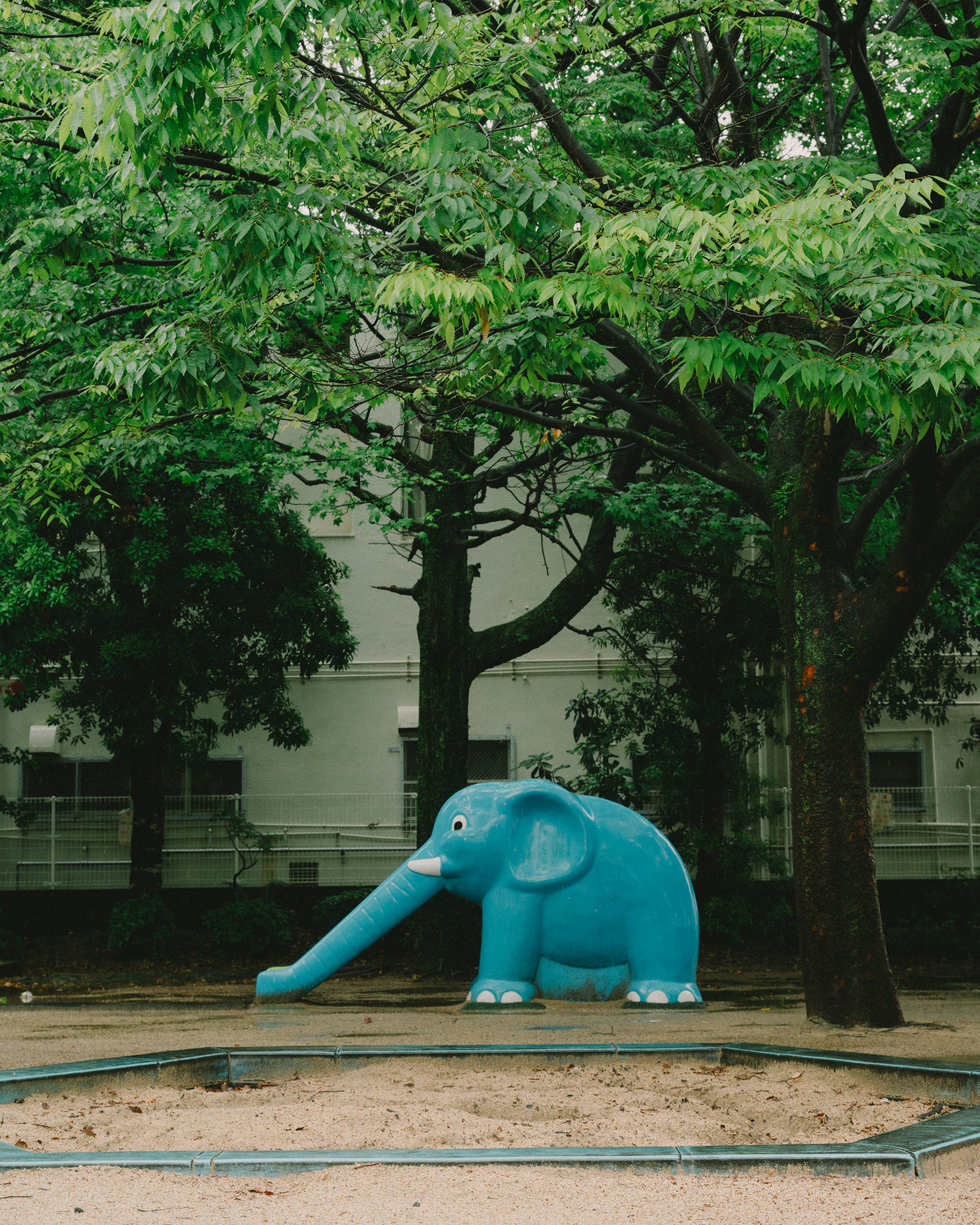 A blue elephant playground structure surrounded by green trees