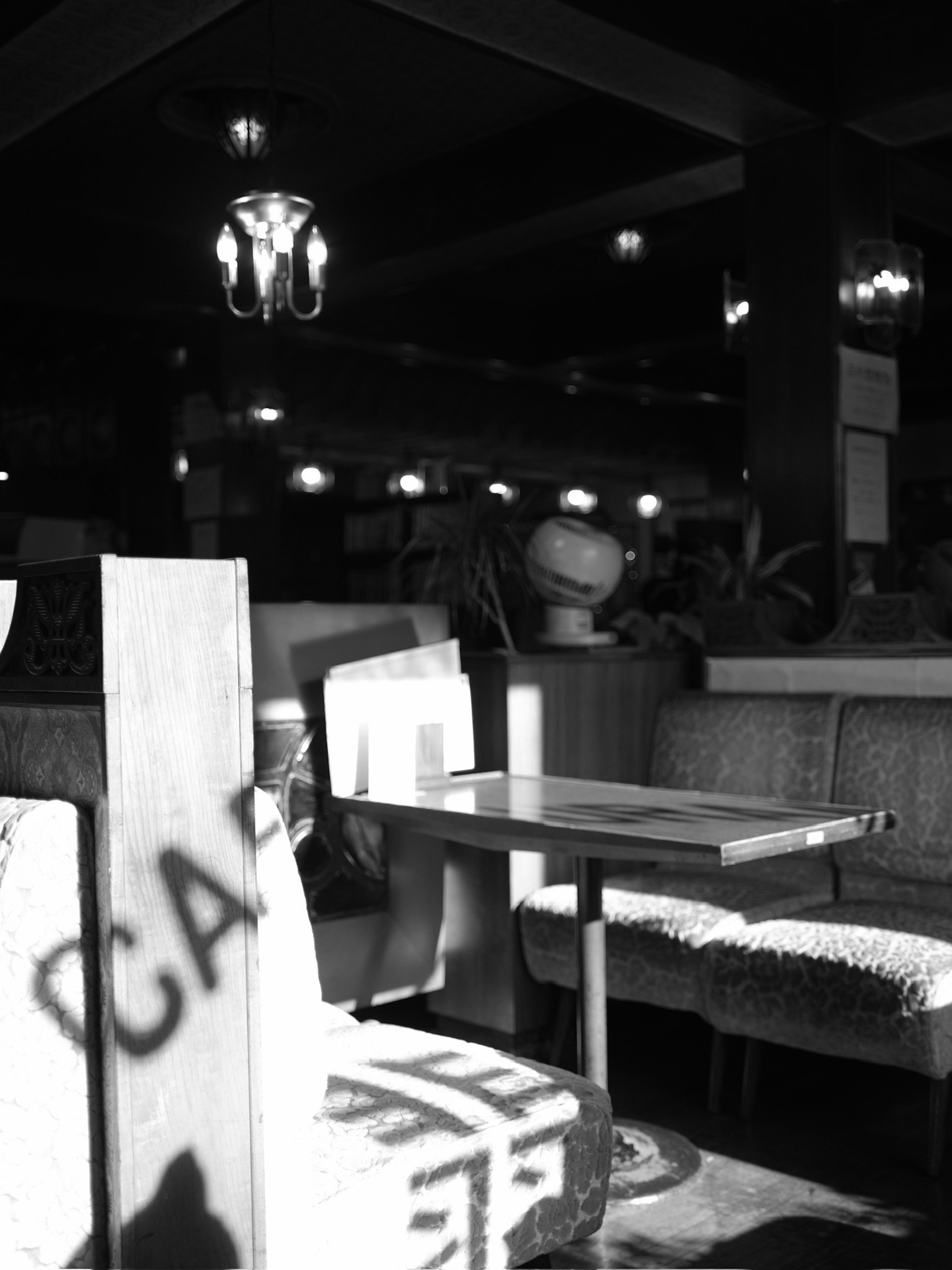 Photo en noir et blanc d'un intérieur de café avec une table et des chaises projetant des ombres