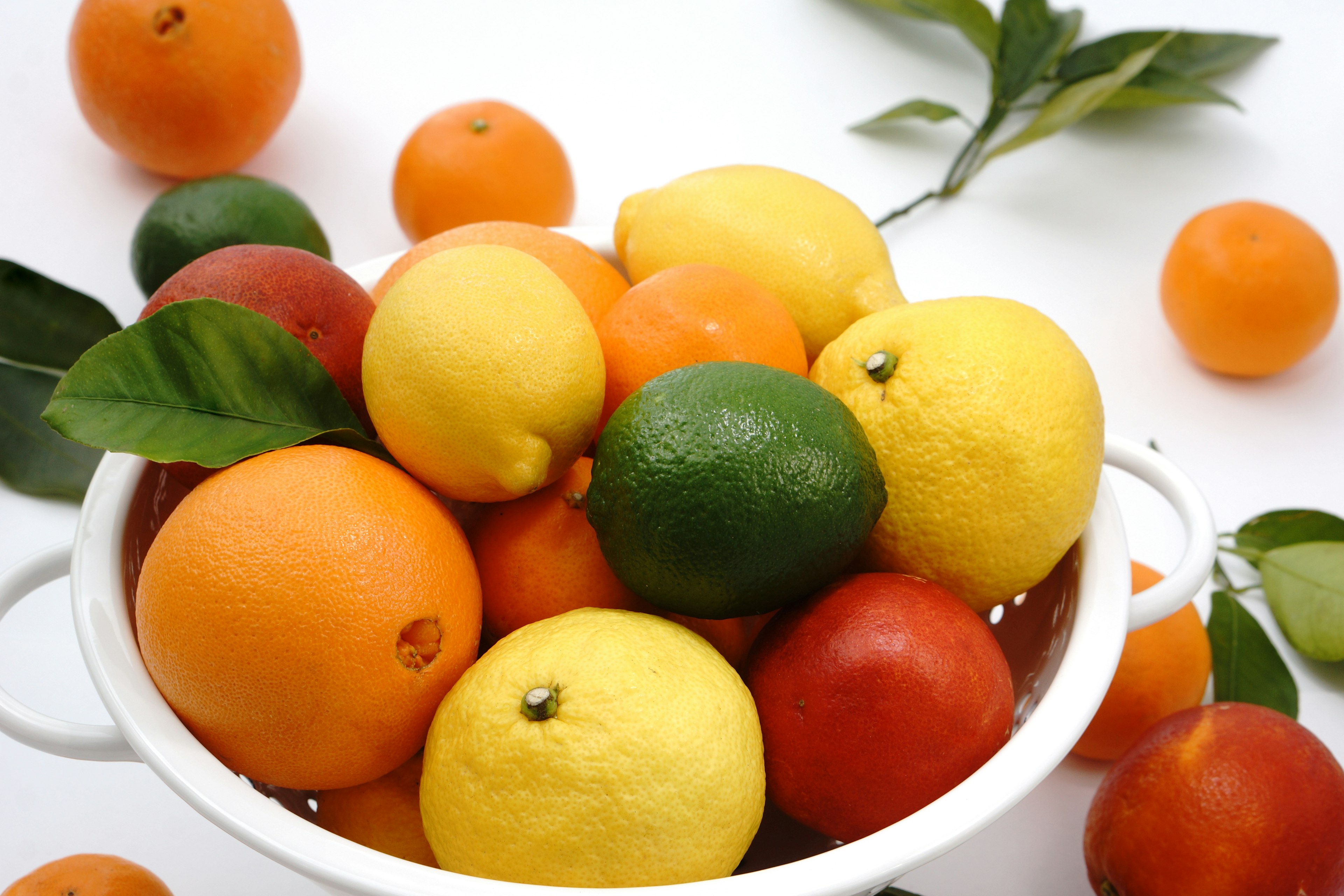 Uno scolapasta pieno di frutti agrumi colorati su sfondo bianco