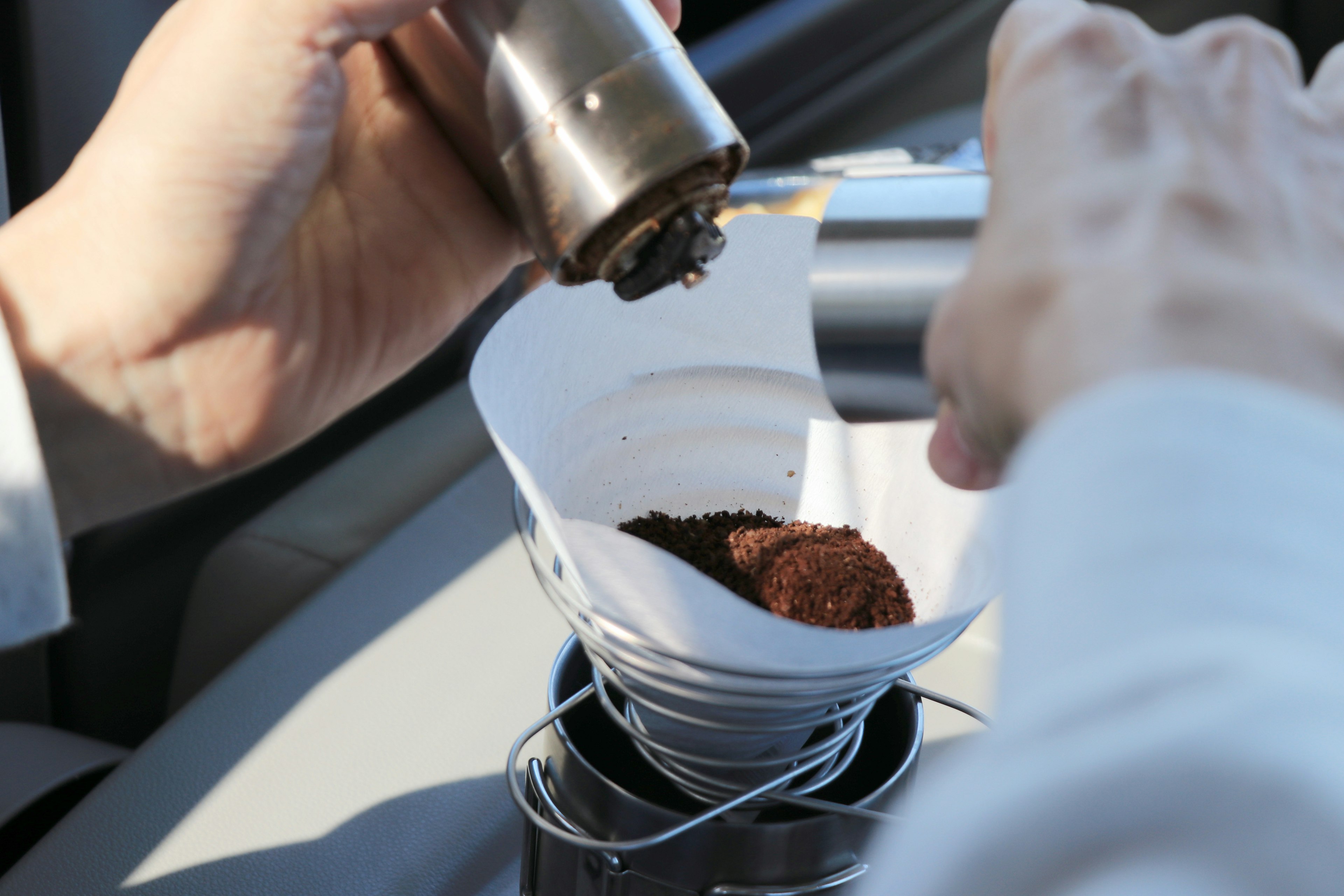 Primo piano di mani che versano caffè macinato in un filtro per preparare caffè