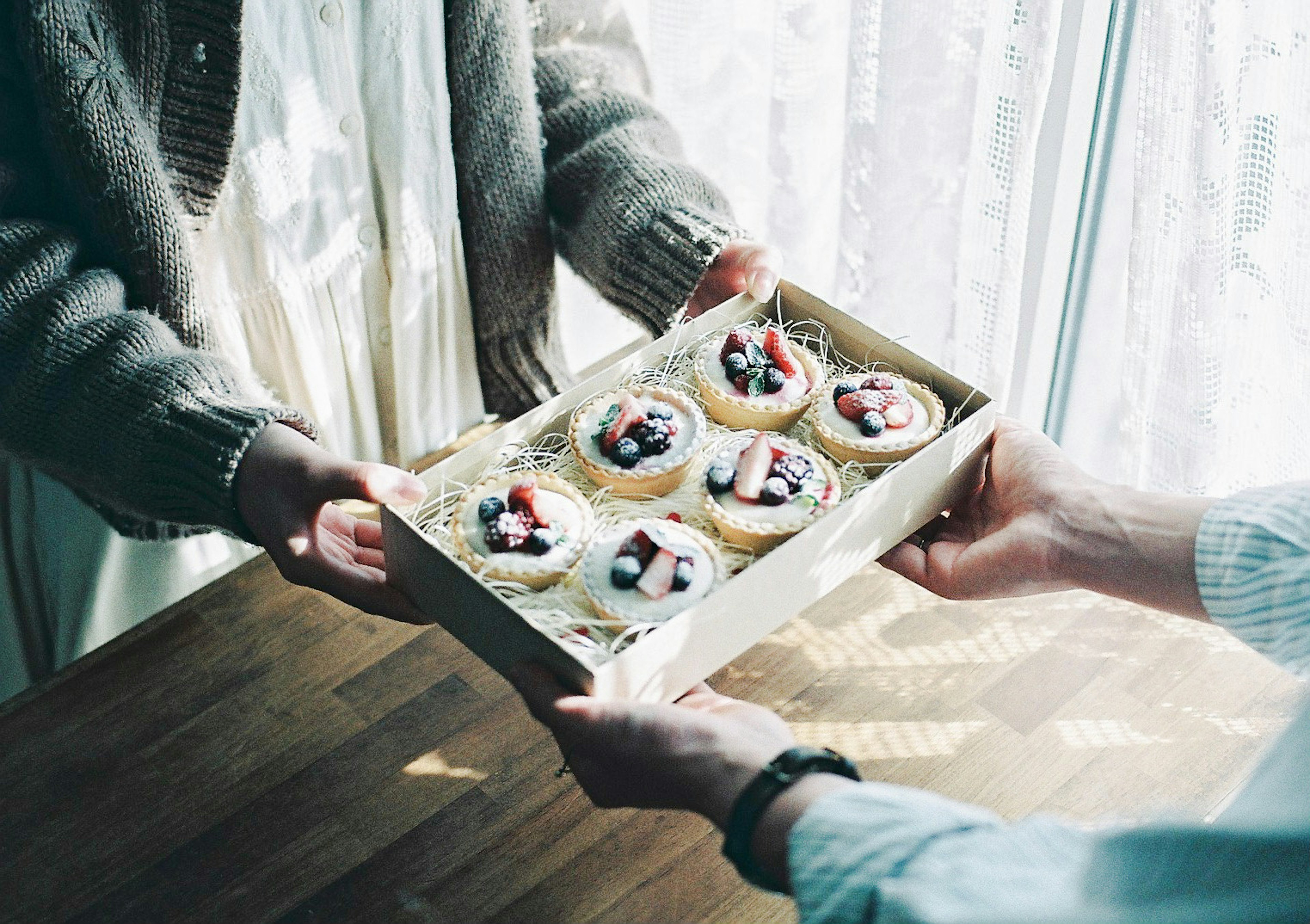 Due mani che scambiano una scatola di dolci con guarnizioni di frutta