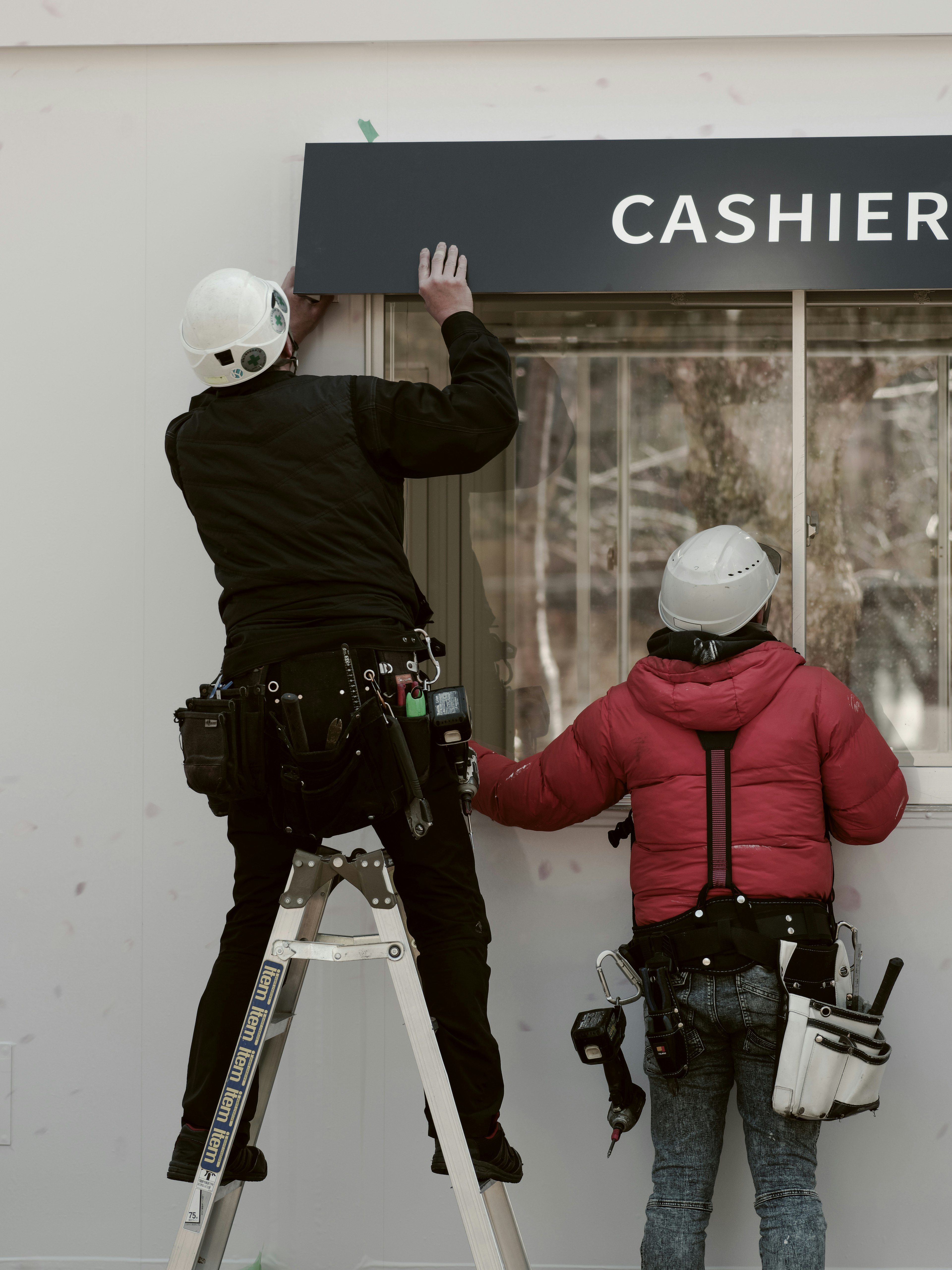 Des travailleurs installent un panneau avec l'inscription CAISSIER sur un mur avec une échelle