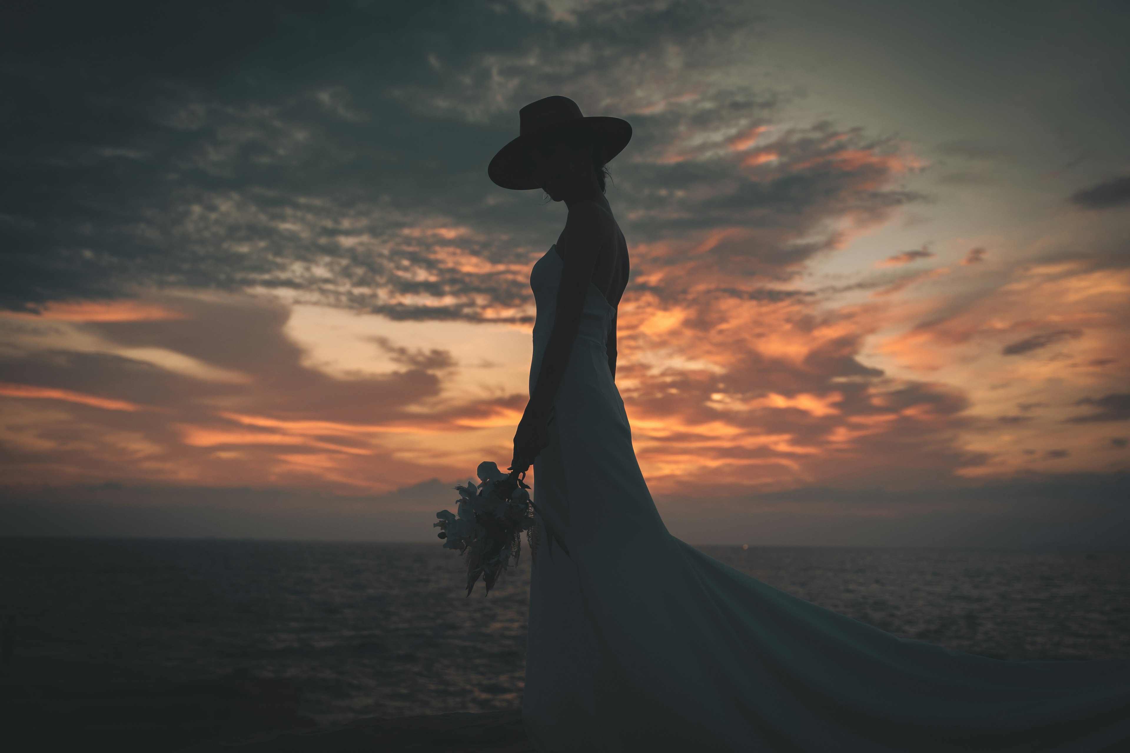 Silhouette of a bride holding a bouquet against a sunset sky