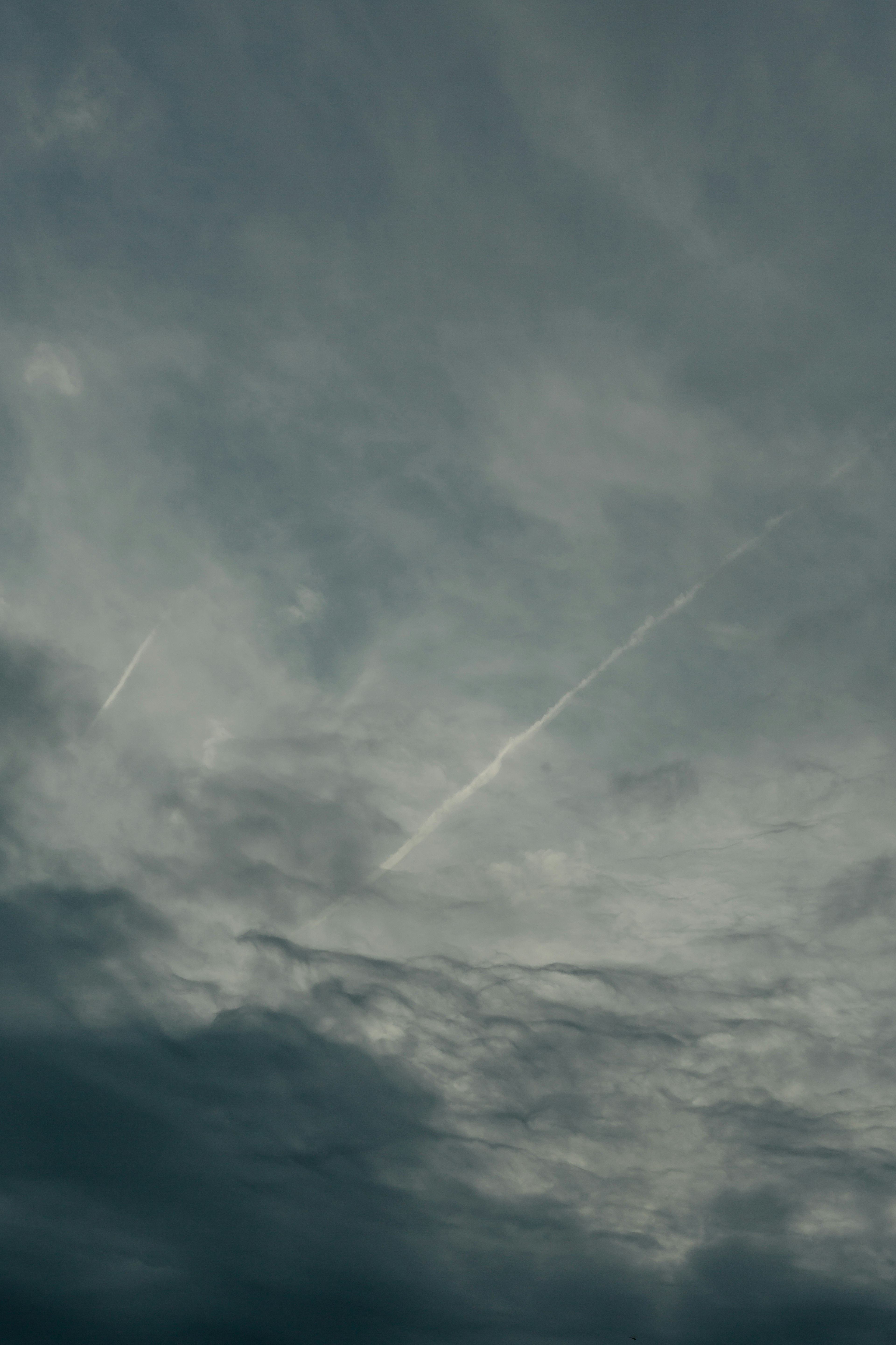 曇り空に薄い雲と飛行機雲が見える風景