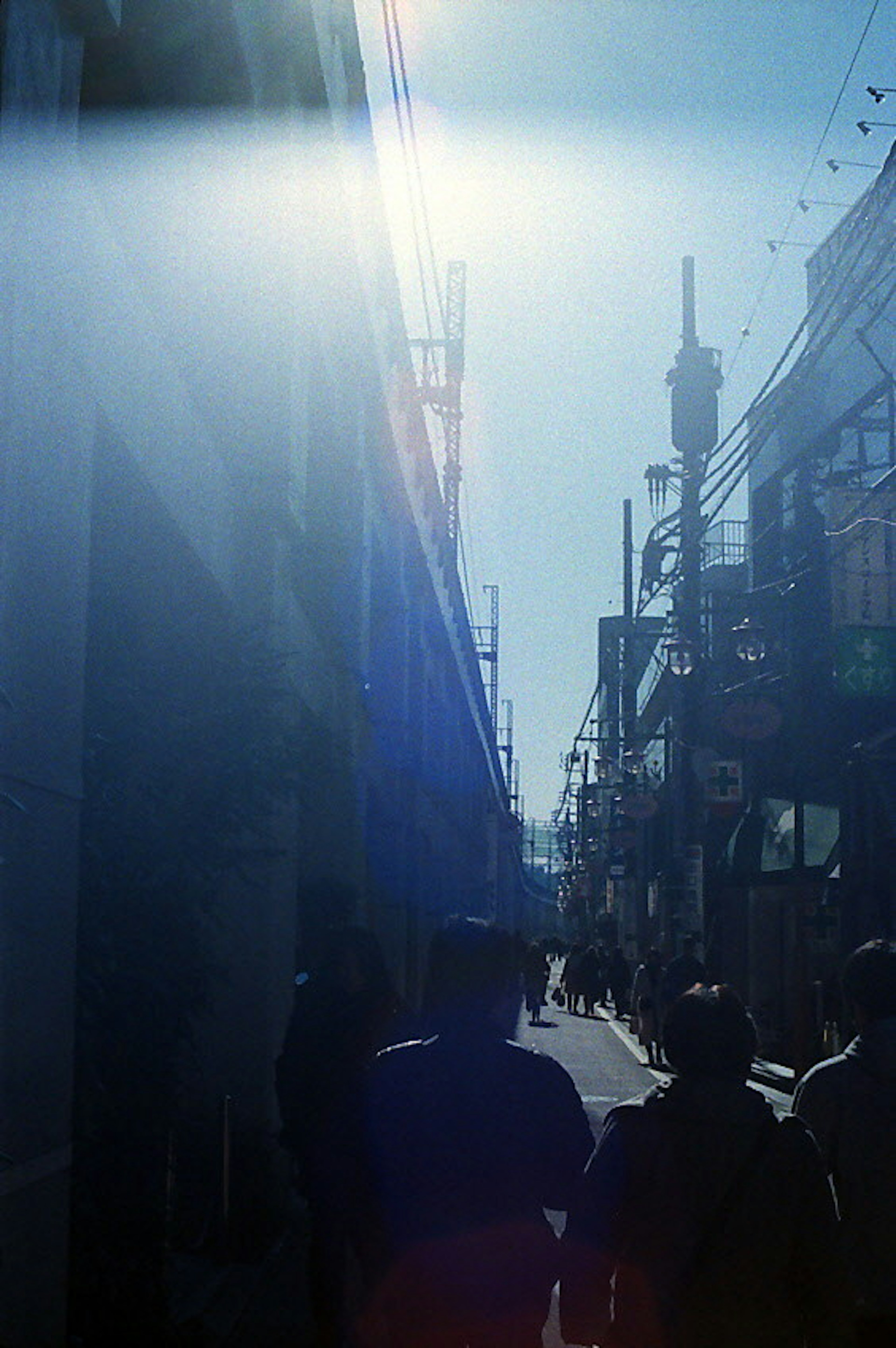 Siluetas de personas caminando por una calle bajo un cielo azul con edificios altos