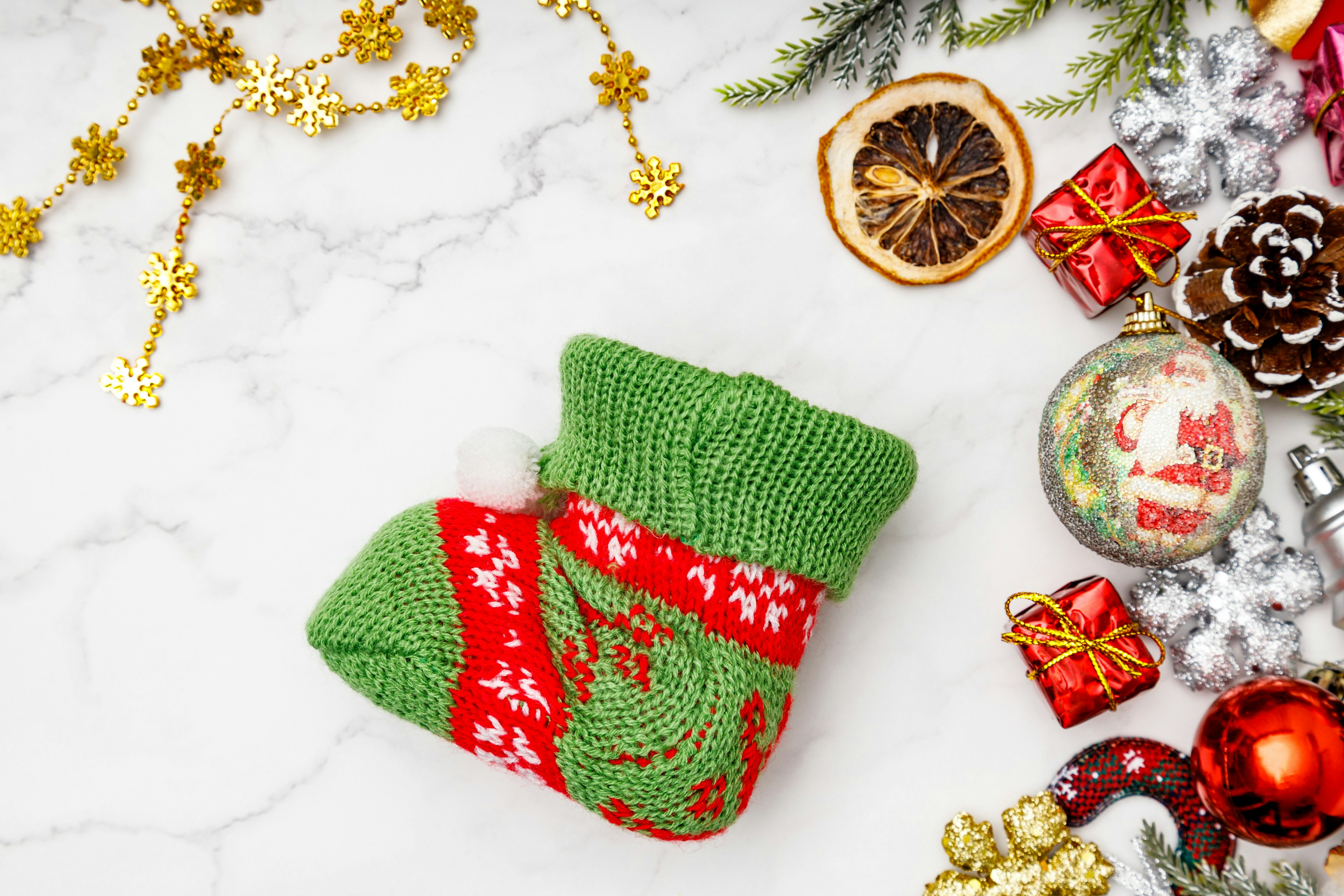 A Christmas-themed knitted sock in green and red colors surrounded by festive ornaments and gifts