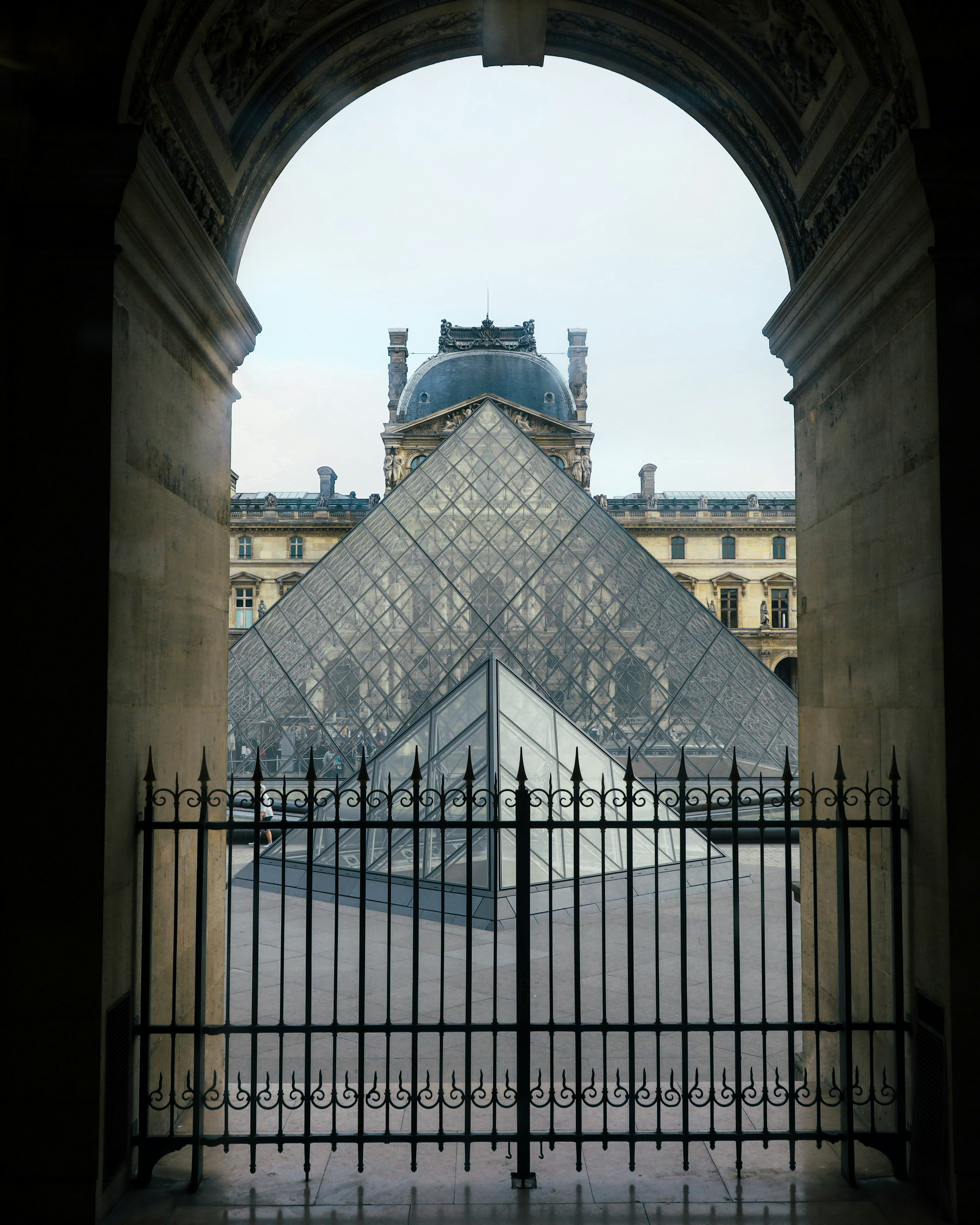 Pemandangan Piramid Louvre melalui pintu melengkung