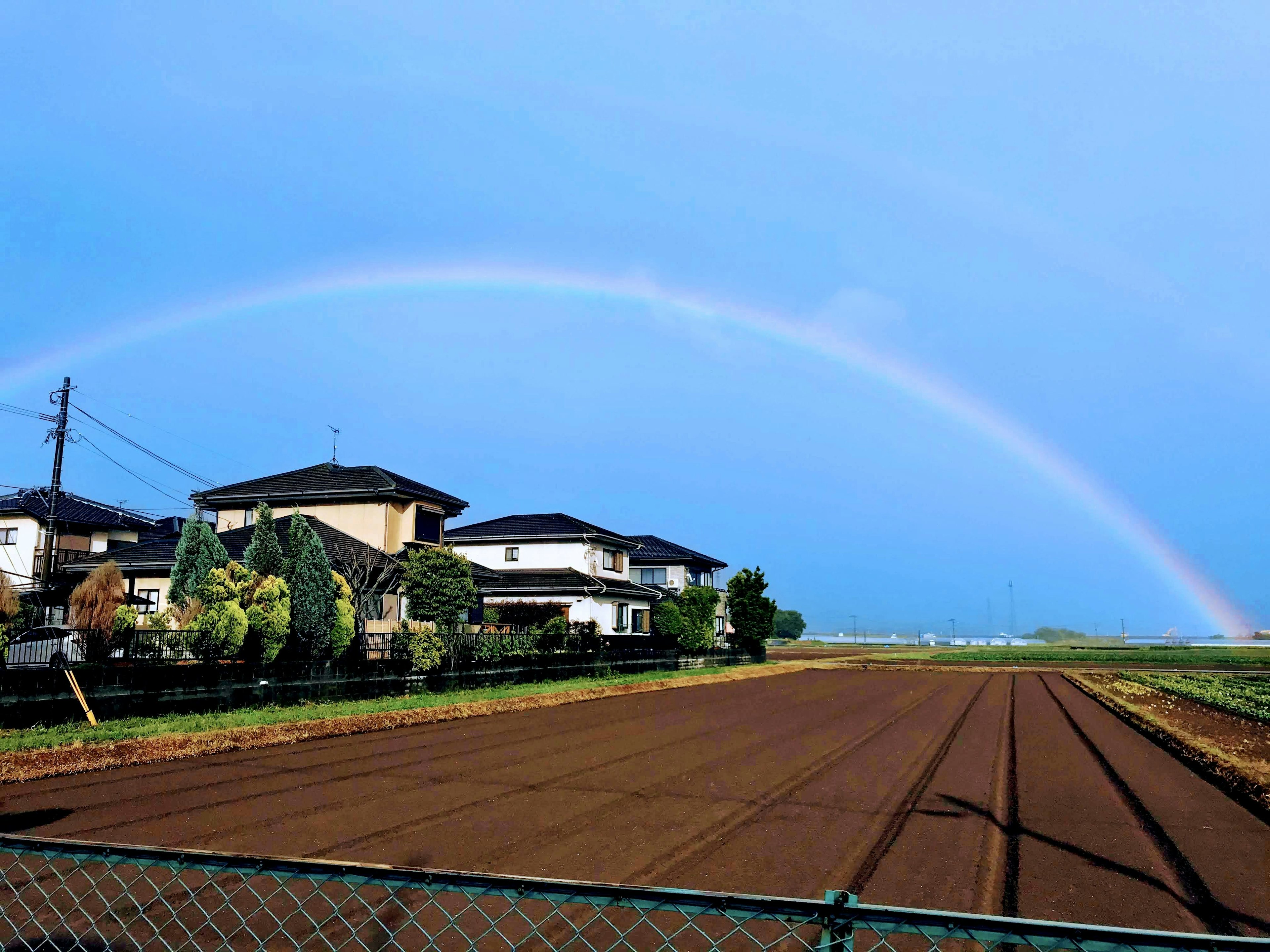 Un arcobaleno sopra un cielo sereno e campi con case lungo il terreno