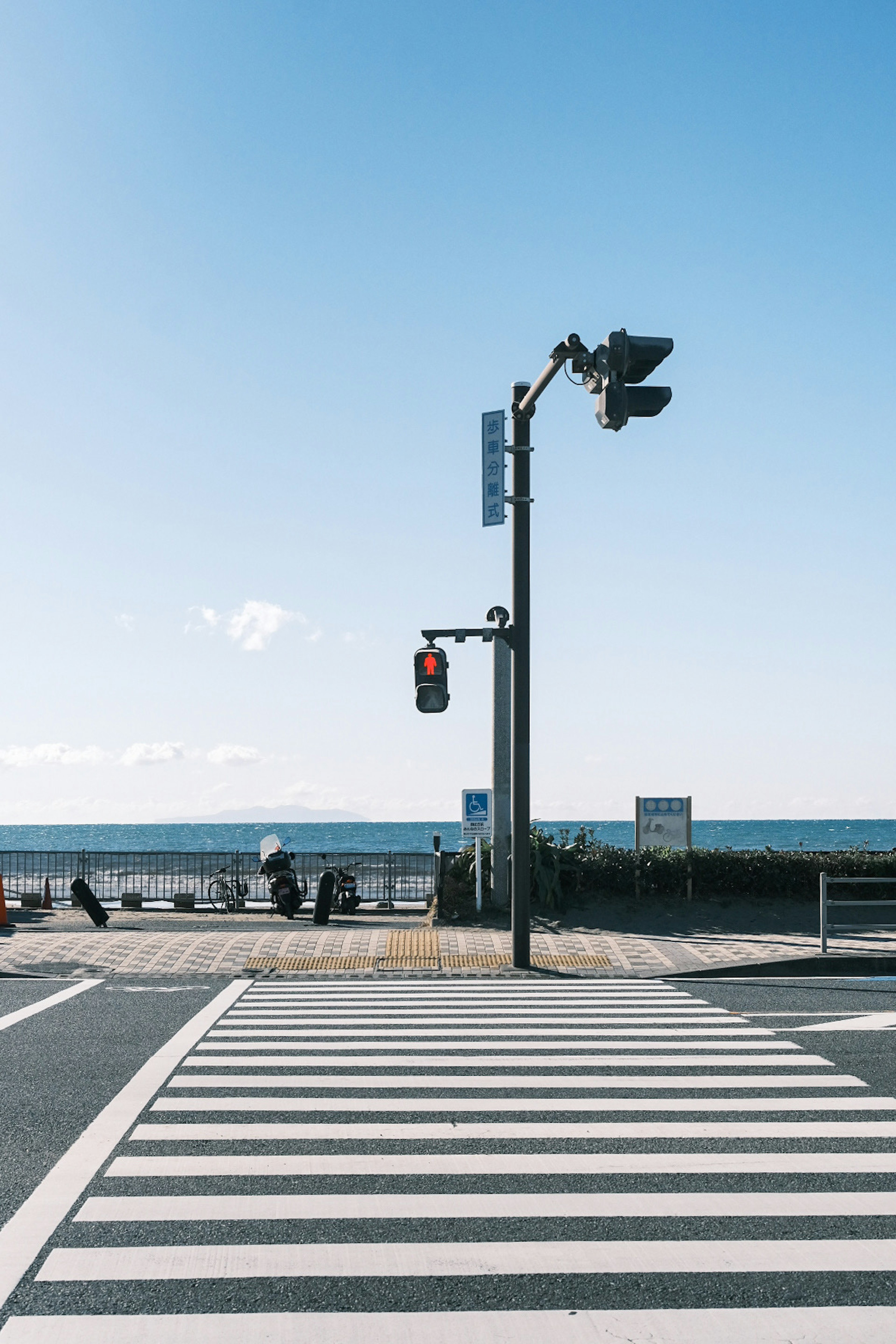 Crosswalk and traffic light near the sea under a clear blue sky