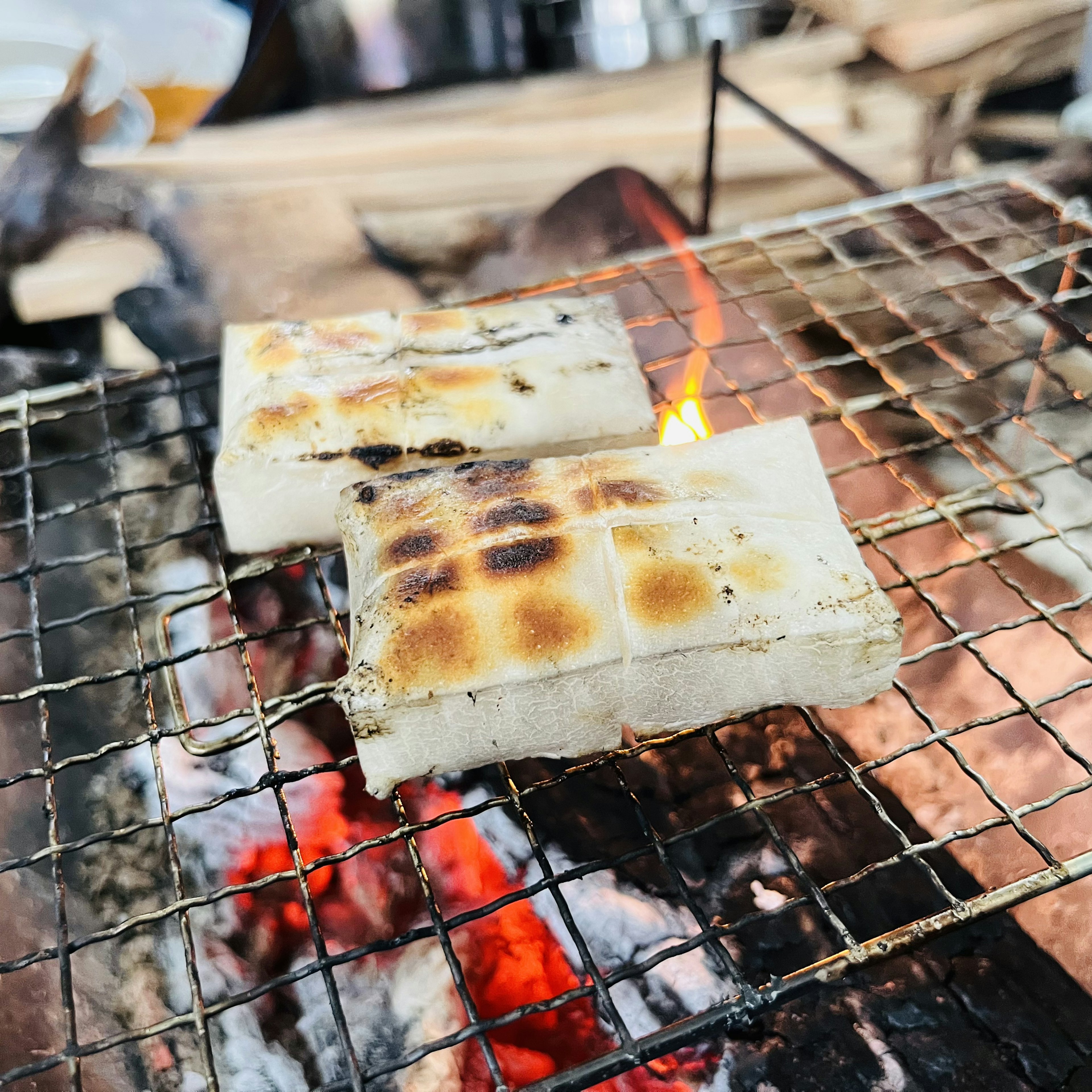 炭火で焼かれた白い食べ物の塊が格子状のグリルの上に置かれている