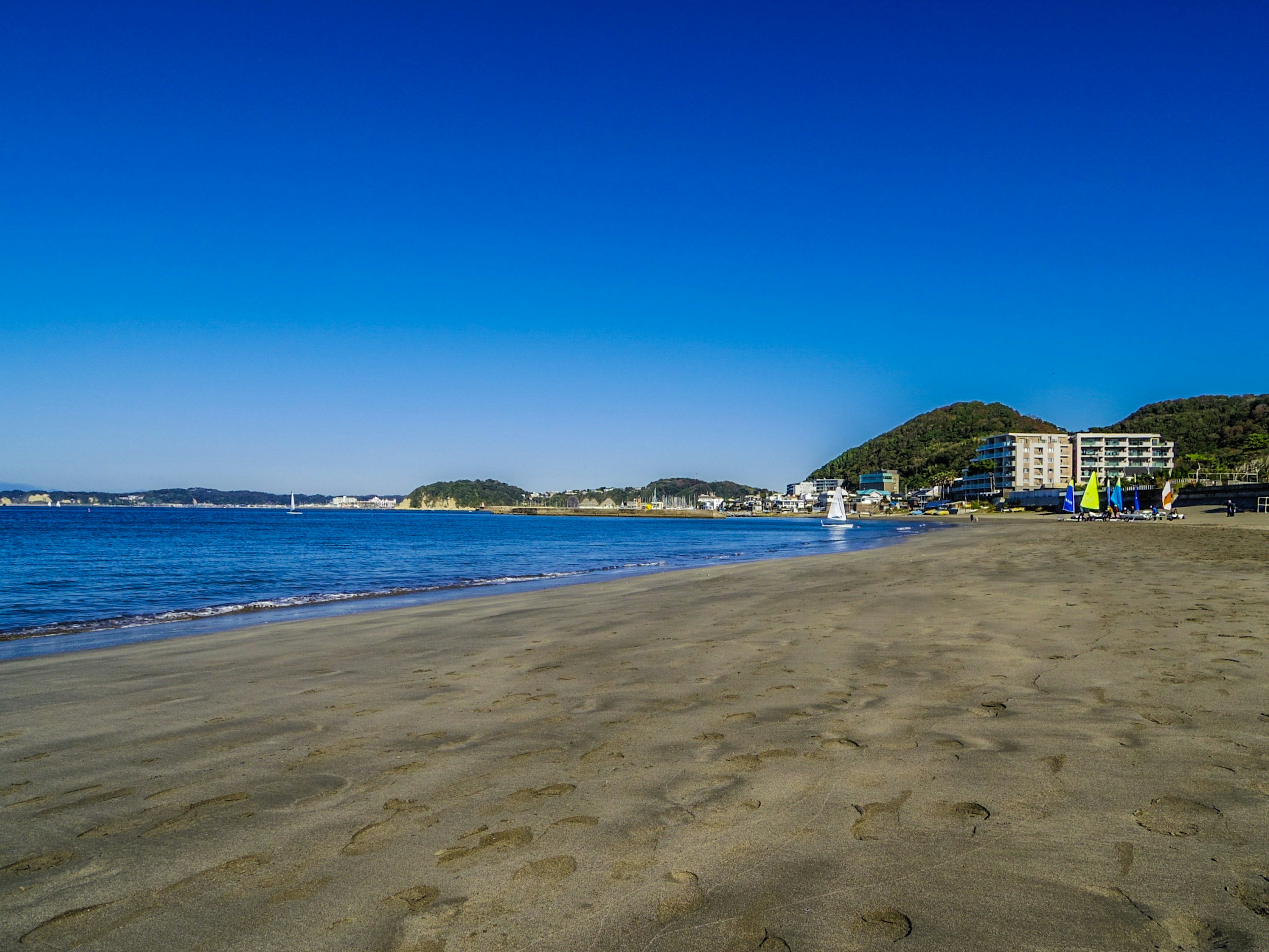 Escena de playa con cielo azul claro y océano playa de arena con edificios a lo lejos