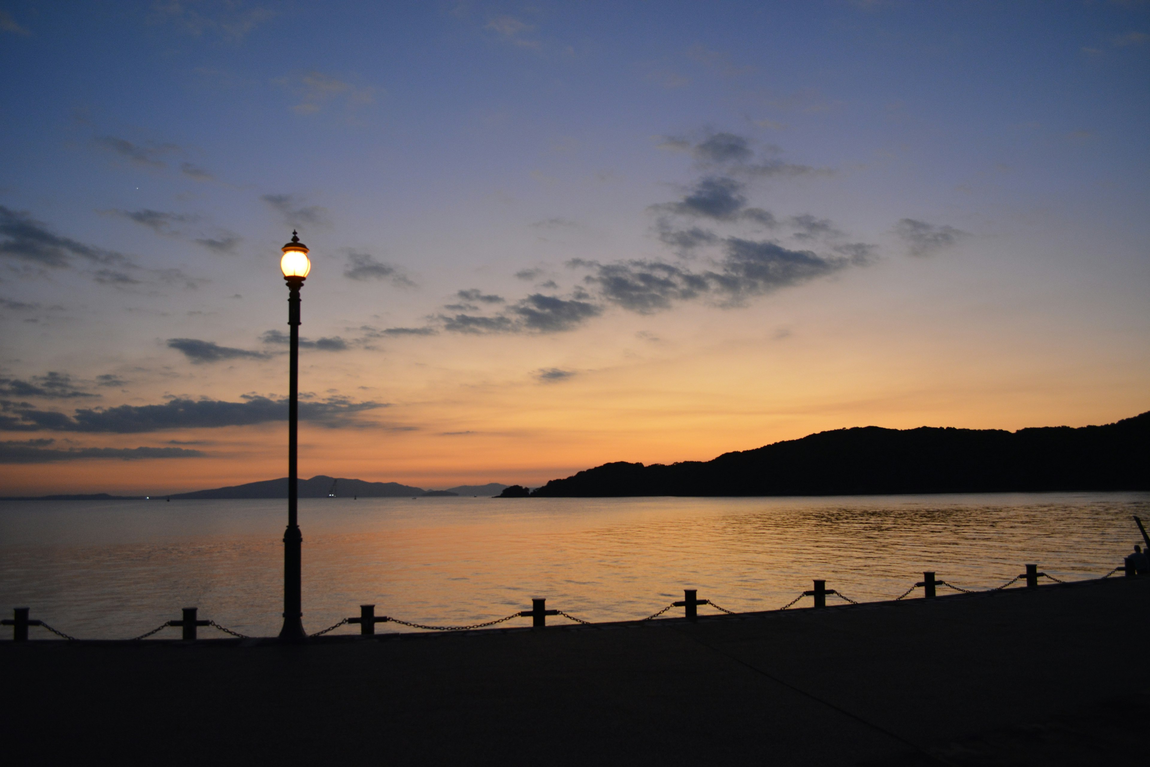 夕焼けの海岸に立つ街灯と穏やかな波