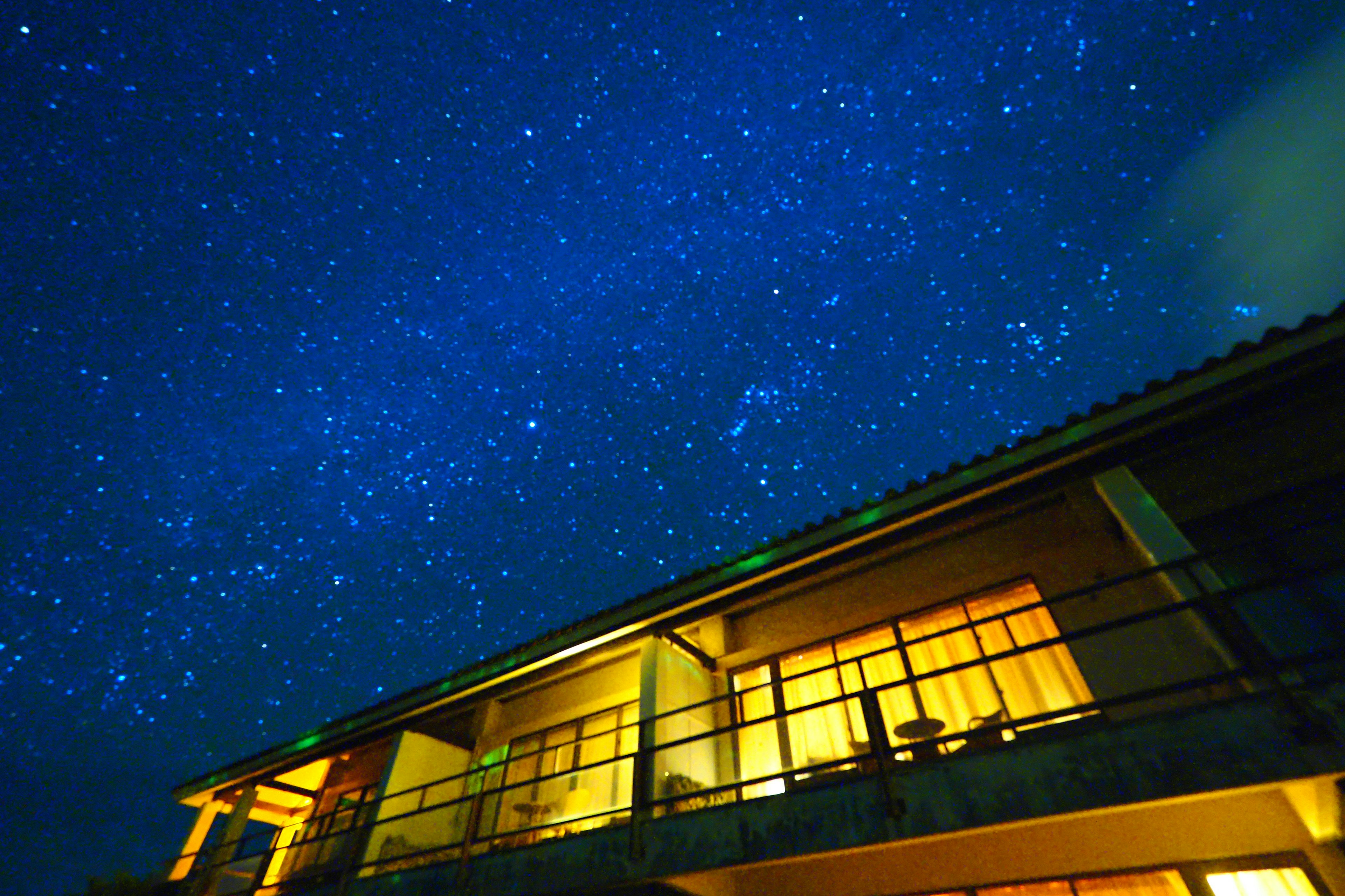 View of a starry night sky above a building with illuminated windows