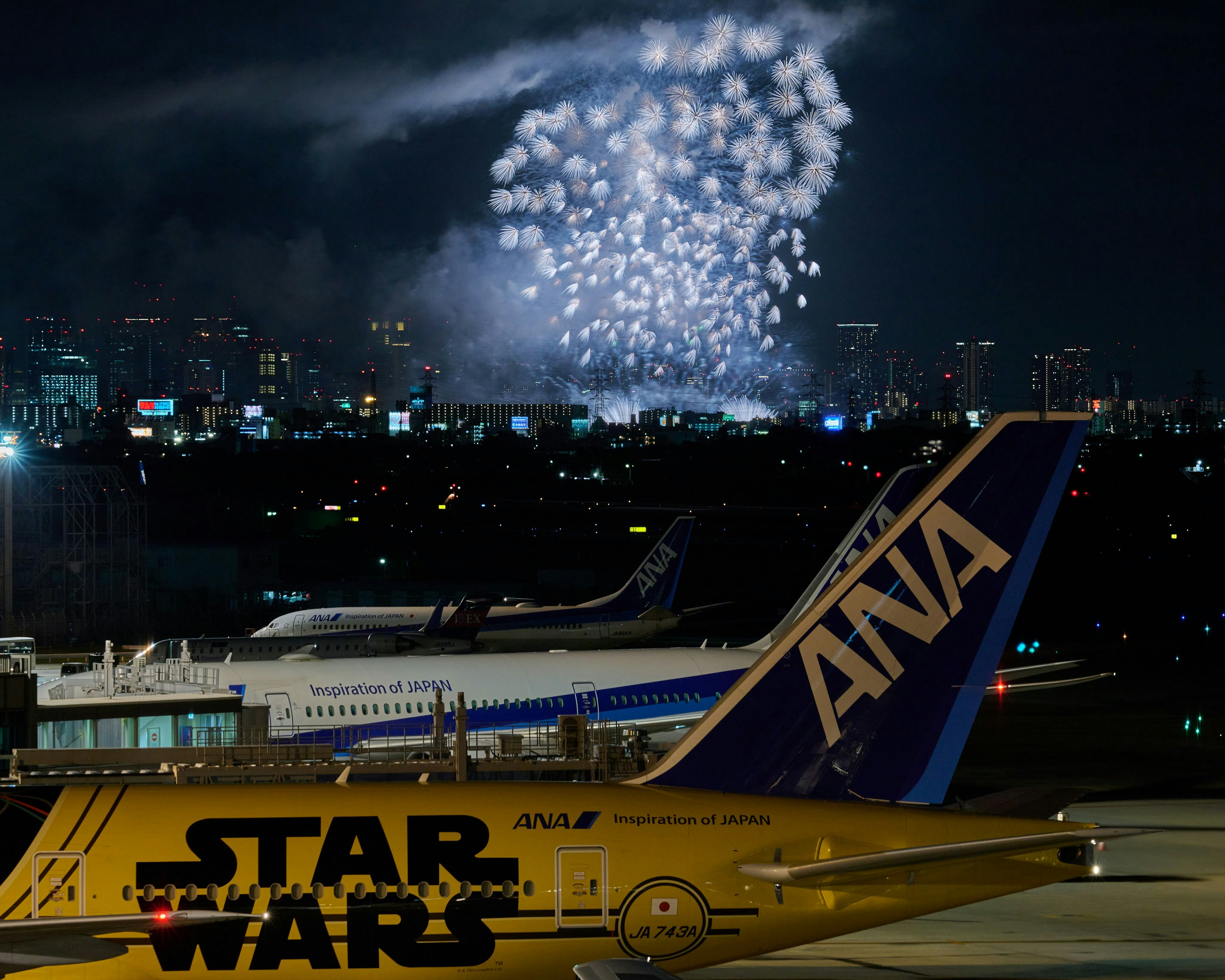 ANA航空機とスター・ウォーズデザインの航空機が夜空の花火の下に並ぶ