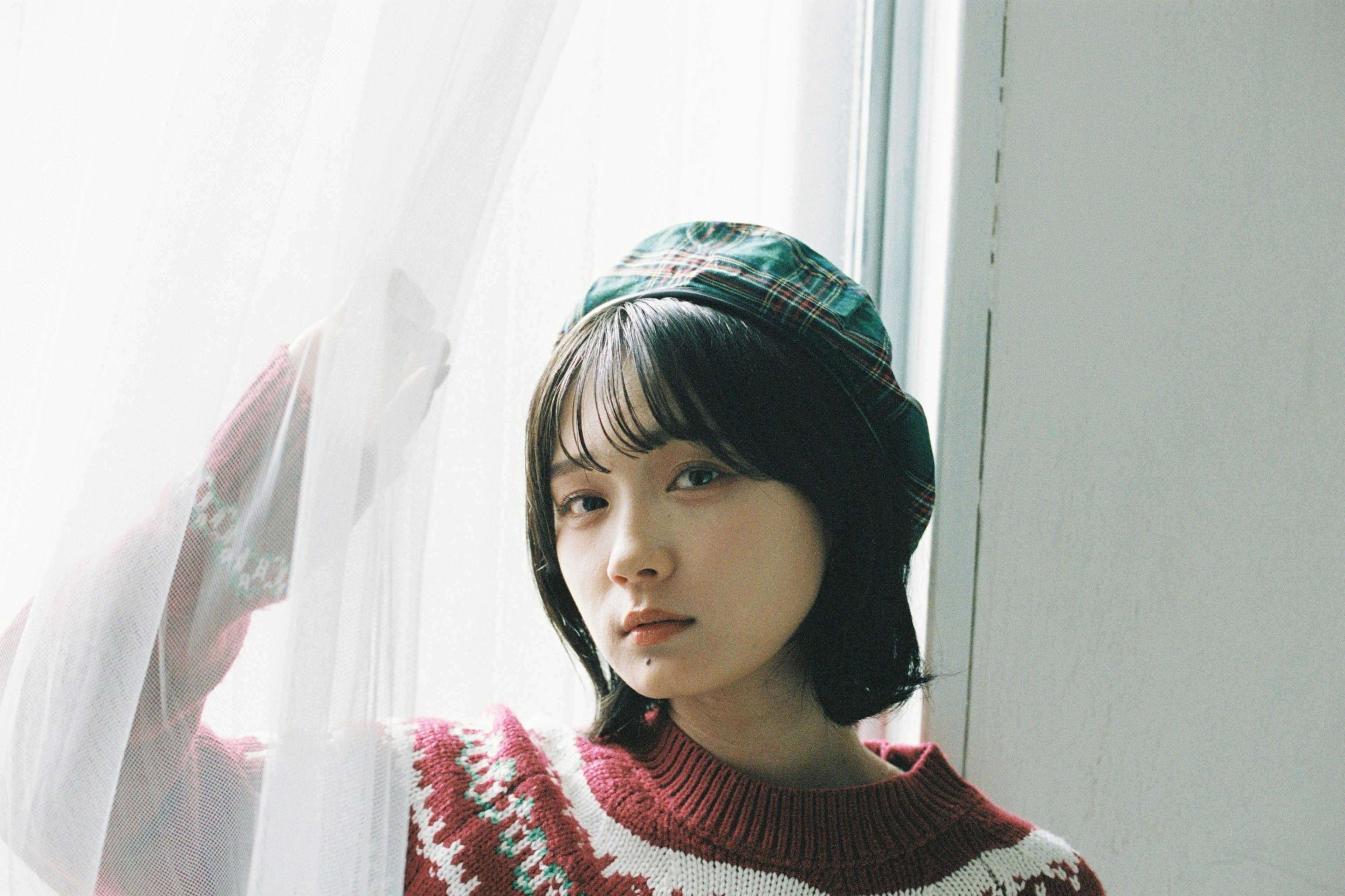 Portrait of a woman standing by the window wearing a red sweater and hat in soft light