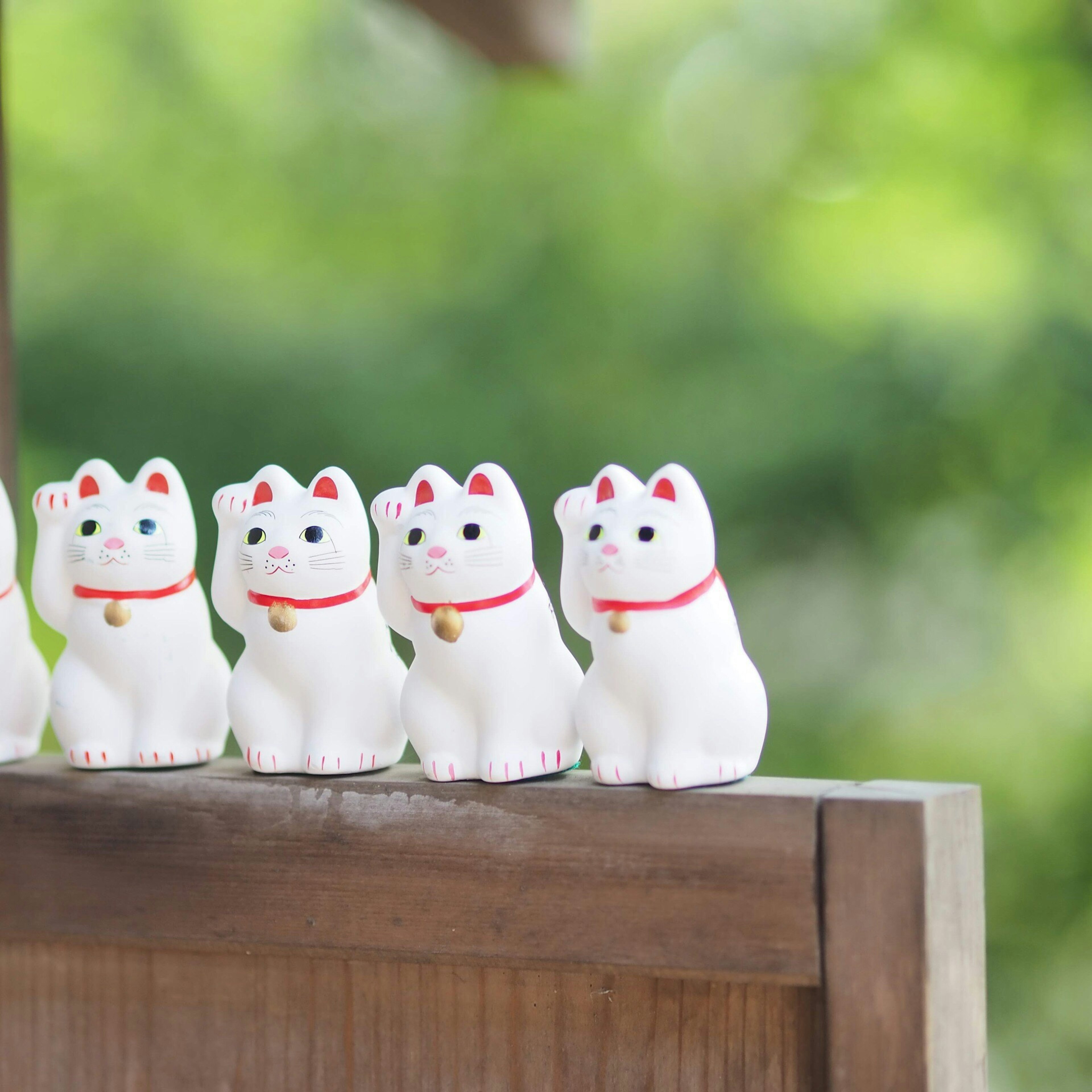 Una fila de pequeñas figuras de gato de la suerte blancas con collares rojos contra un fondo verde