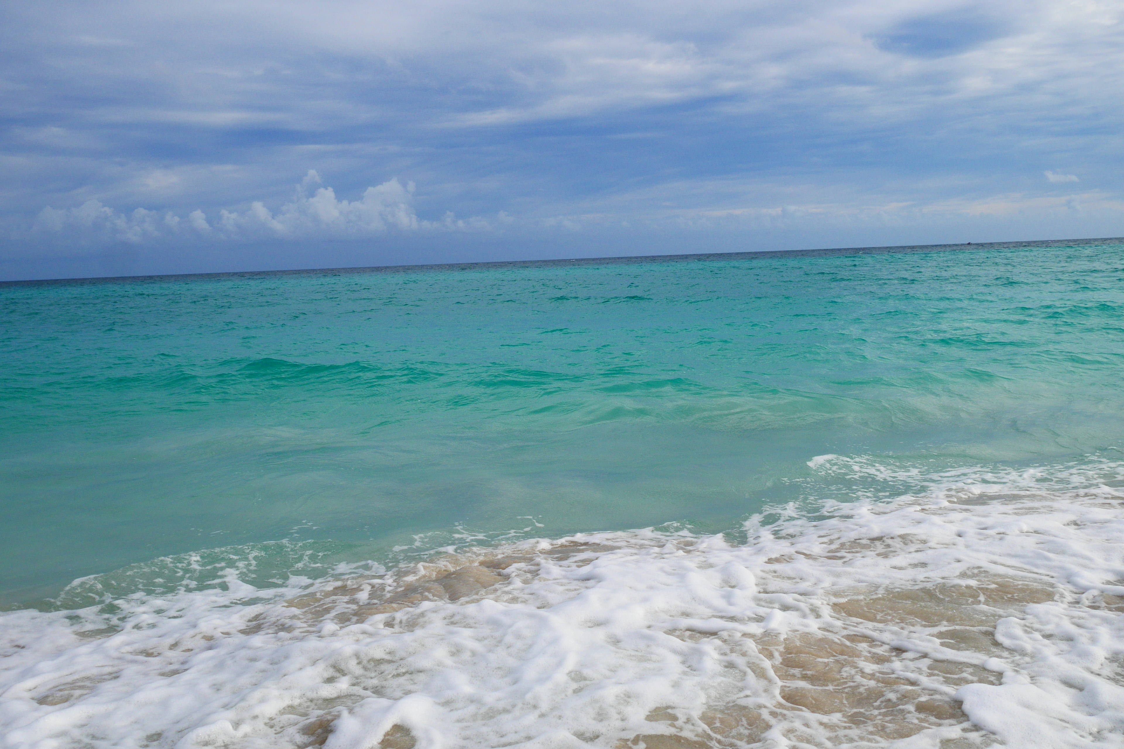 Laut turquoise jernih dengan gelombang lembut di pantai pasir