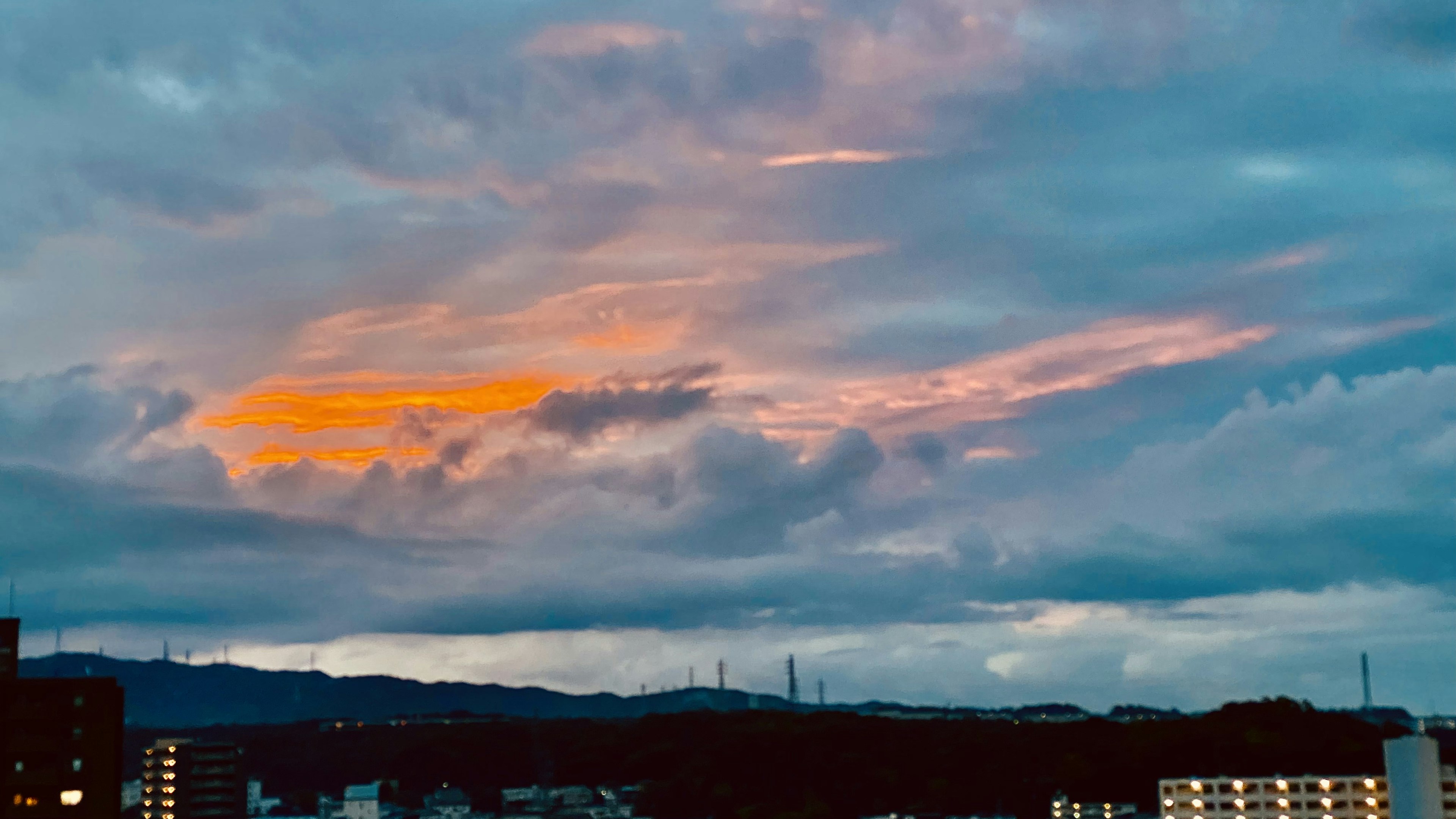 Stadtlandschaft mit bunten Sonnenuntergangs-Wolken und Bergen im Hintergrund