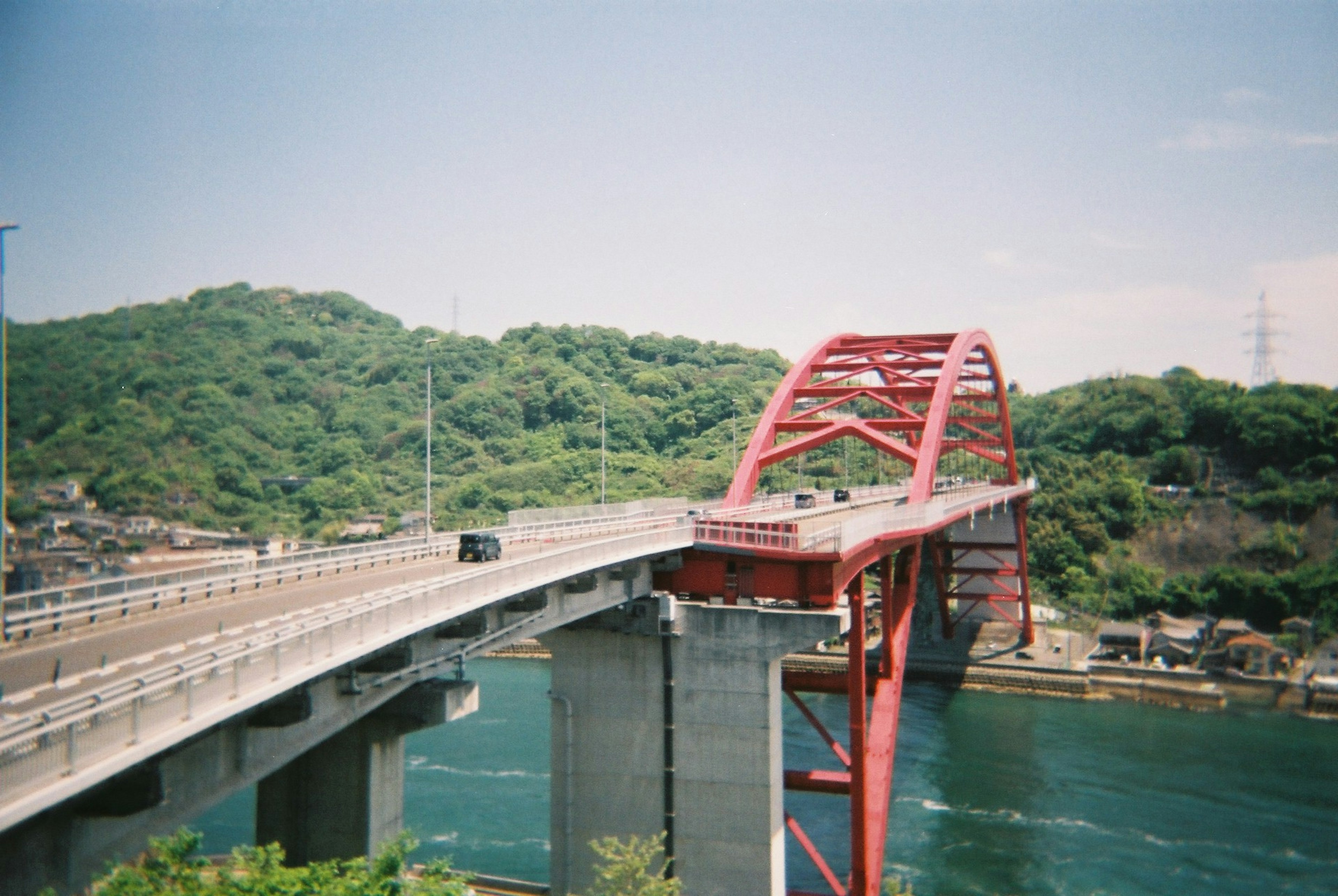 红色拱桥横跨河流，背景是郁郁葱葱的绿色山丘