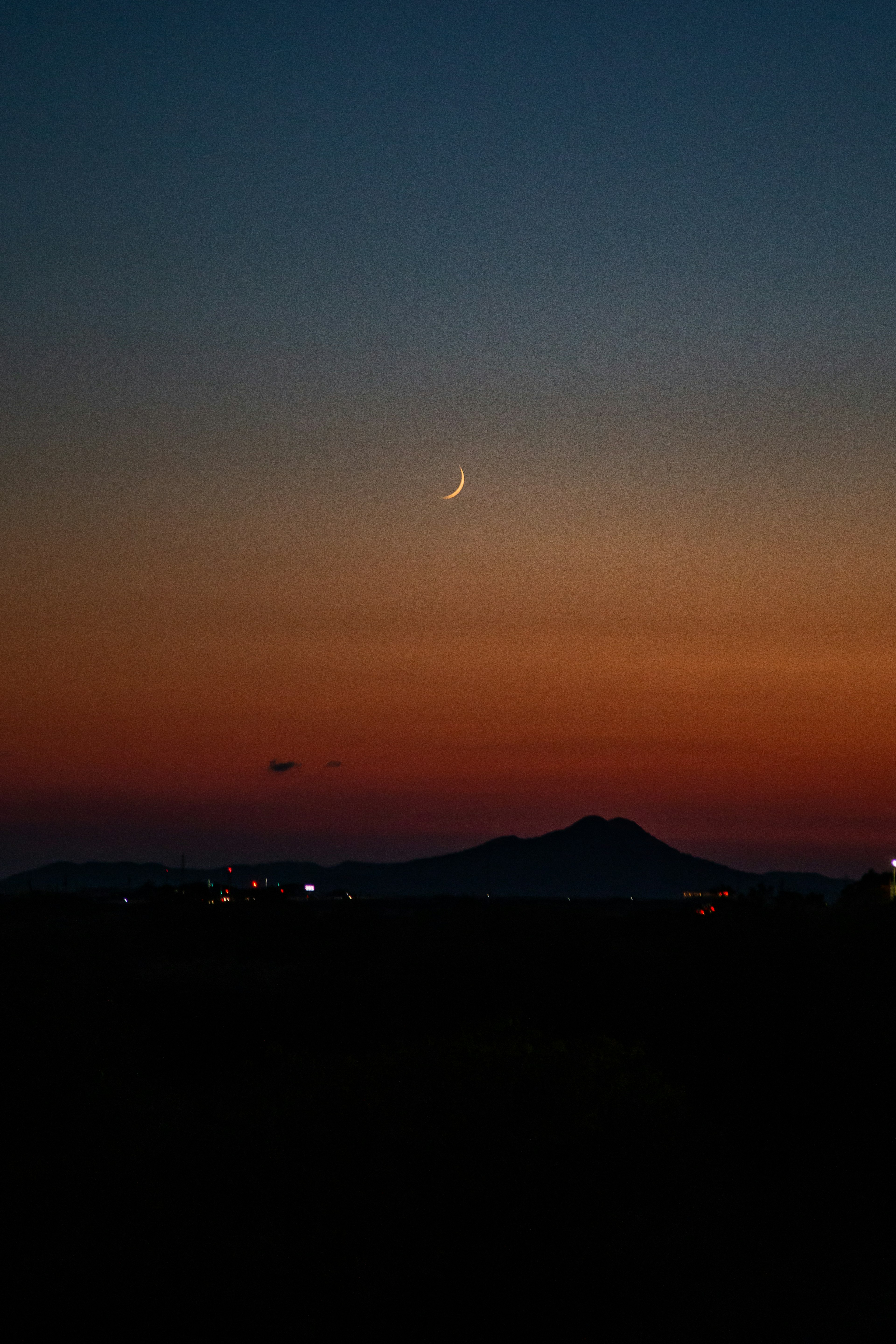 A crescent moon in the twilight sky over a mountain landscape