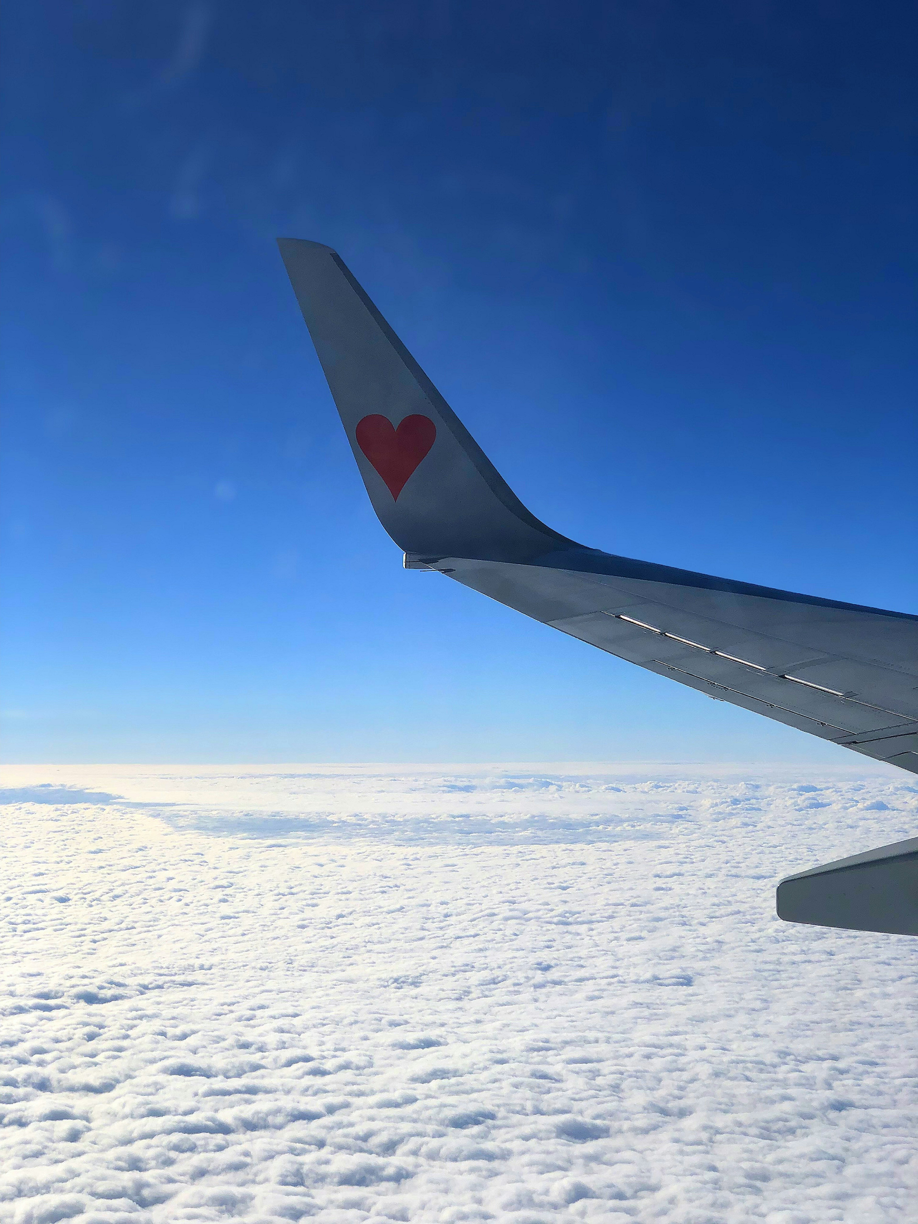 Airplane wing with a red heart logo against a blue sky and clouds