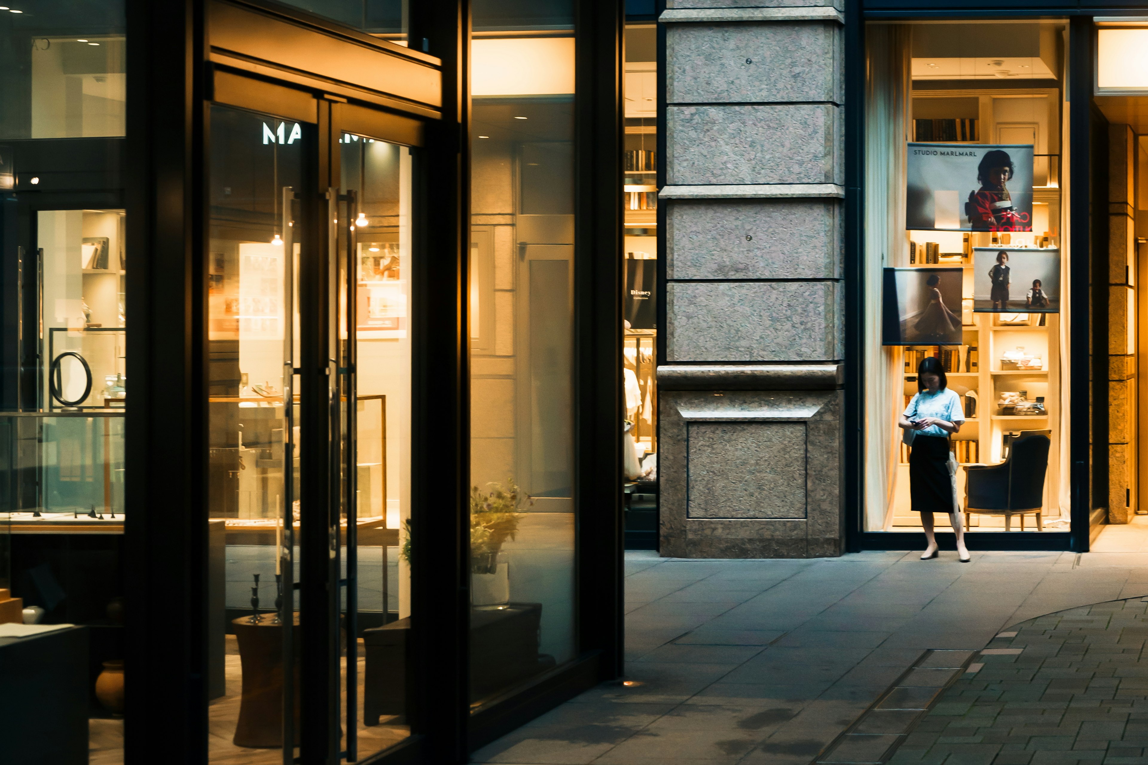 Stylish shopping street at night featuring glass storefronts and art displays