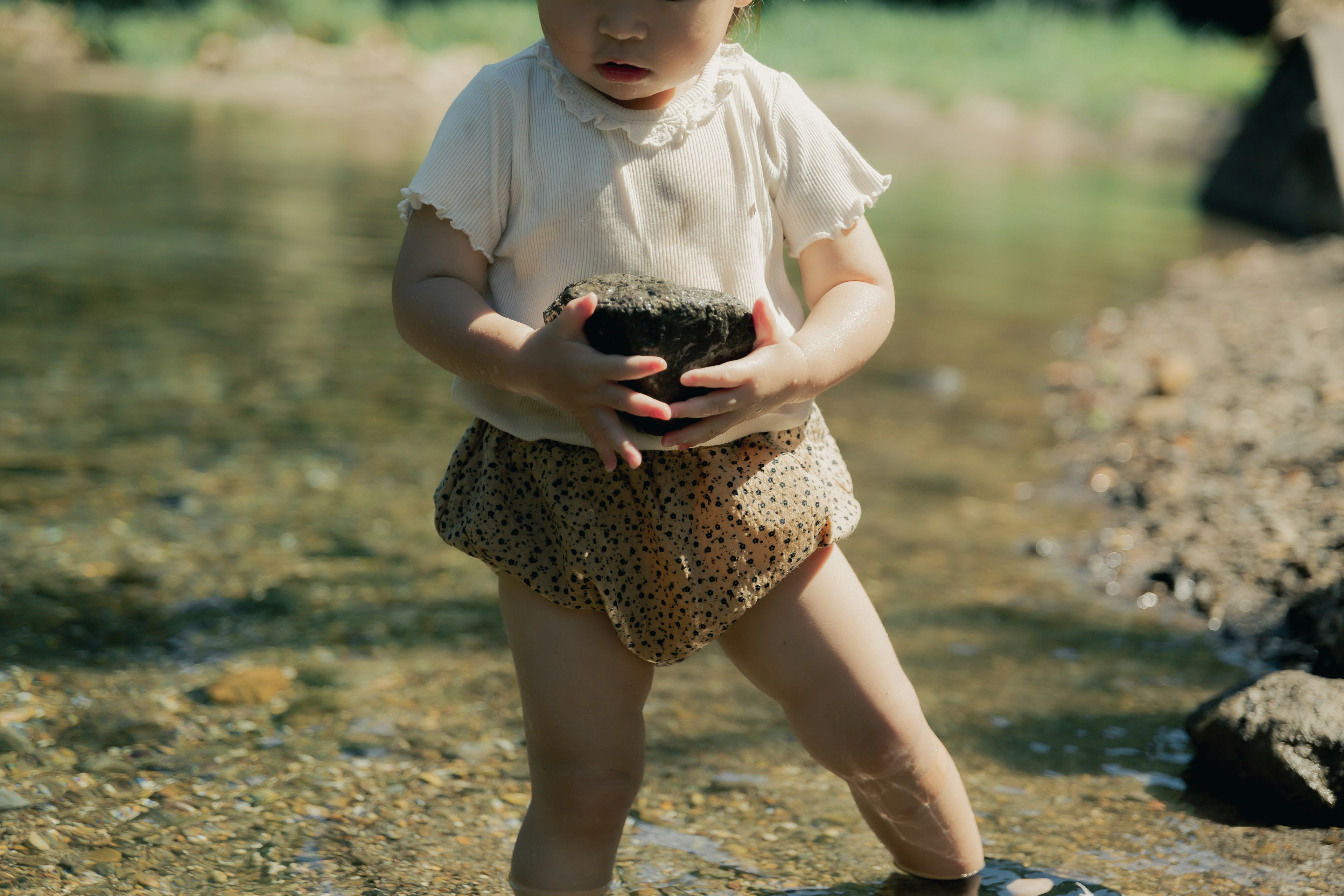 Ein kleines Kind hält einen Stein im flachen Wasser