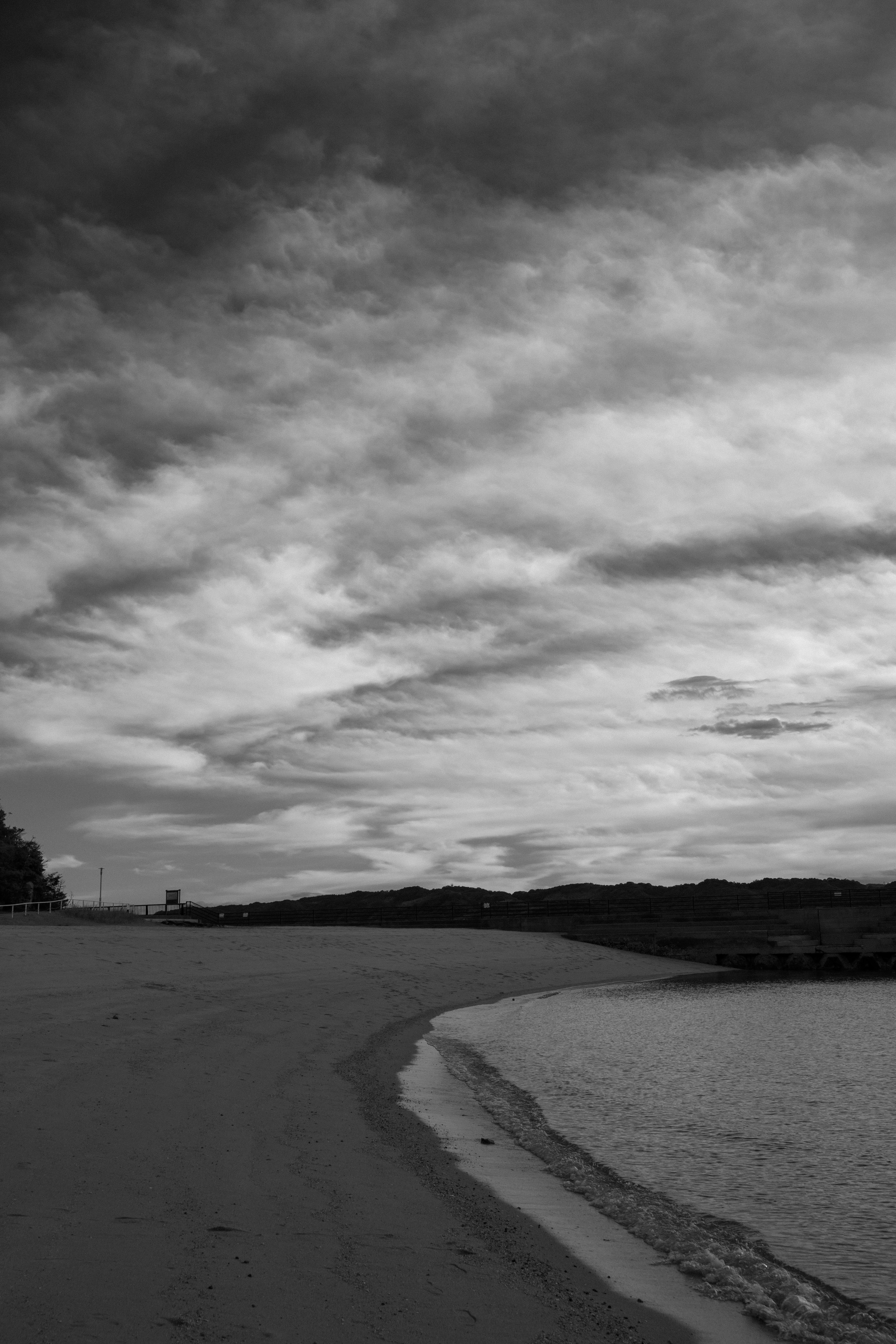 Escena de playa en blanco y negro con olas tranquilas golpeando la arena y un cielo nublado