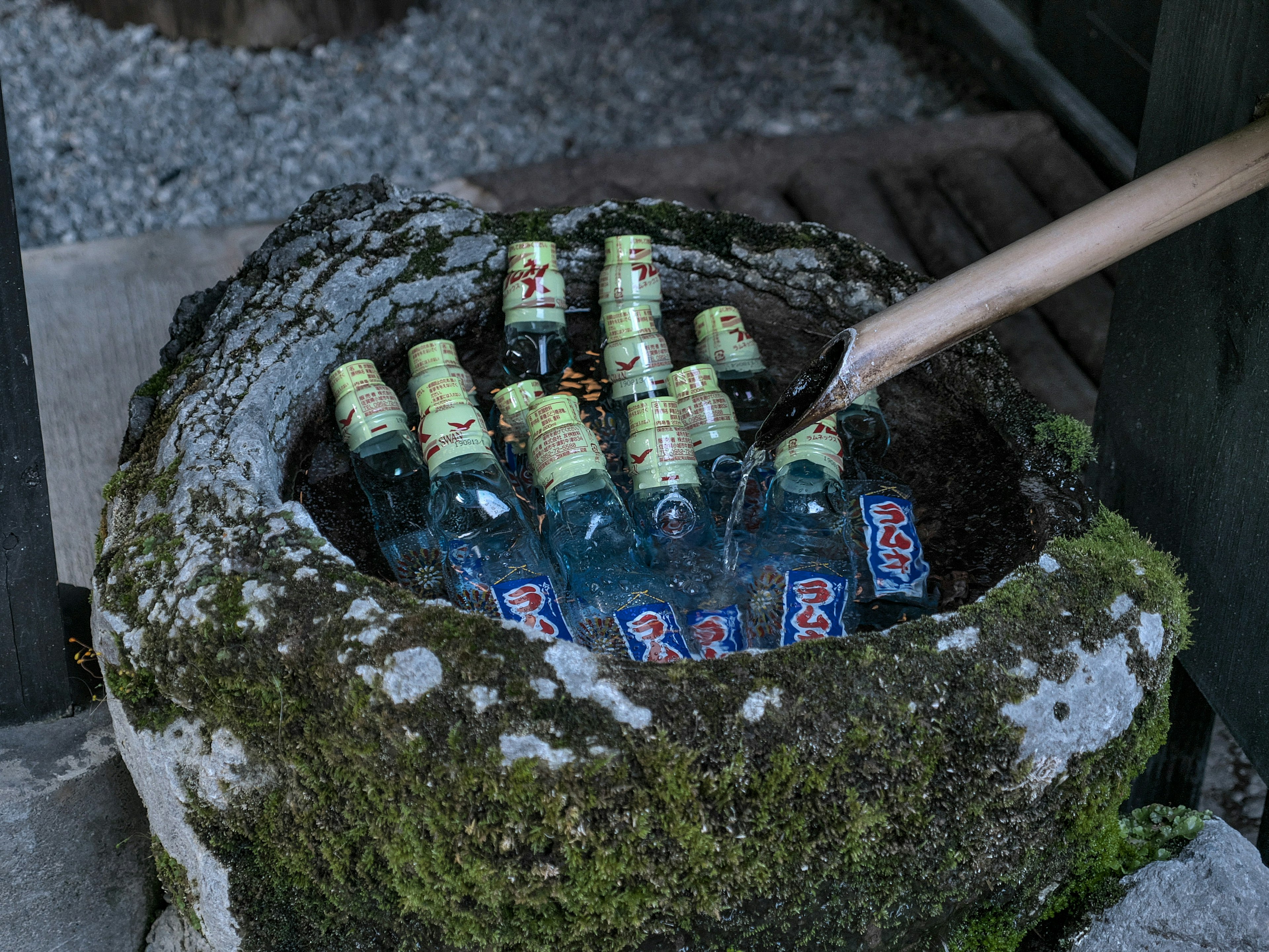 Un recipiente de piedra lleno de agua que contiene varias botellas con etiquetas verdes