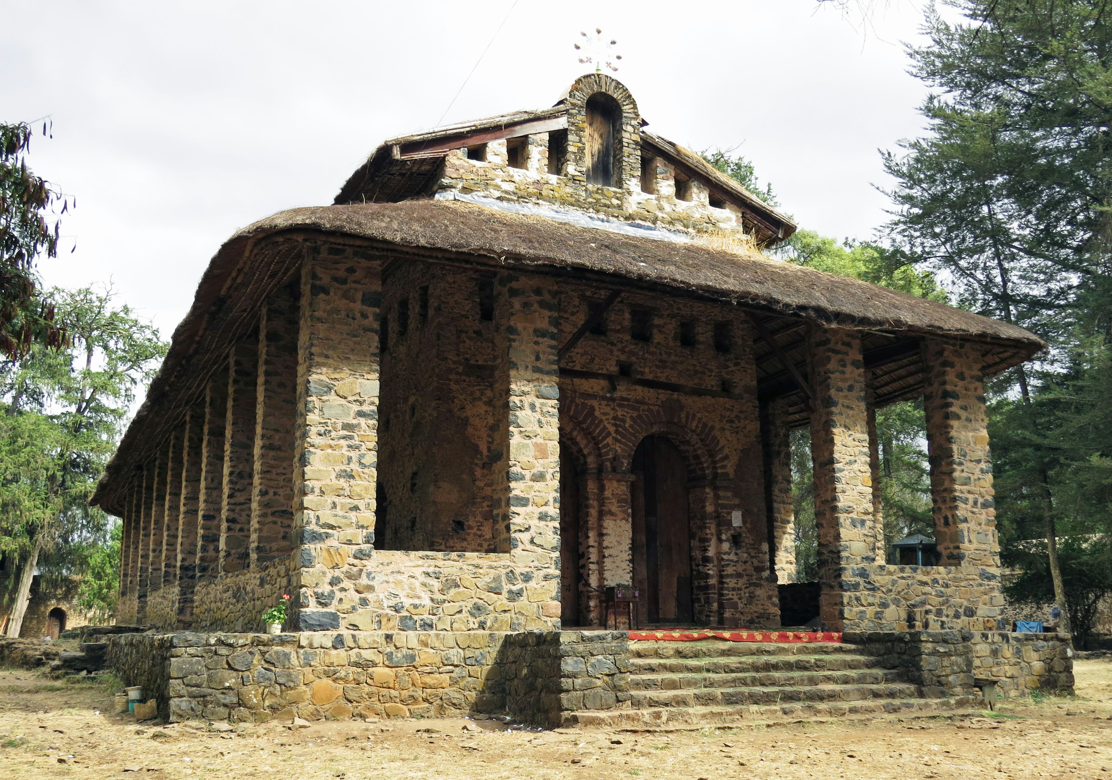 Old stone building with a thatched roof surrounded by trees