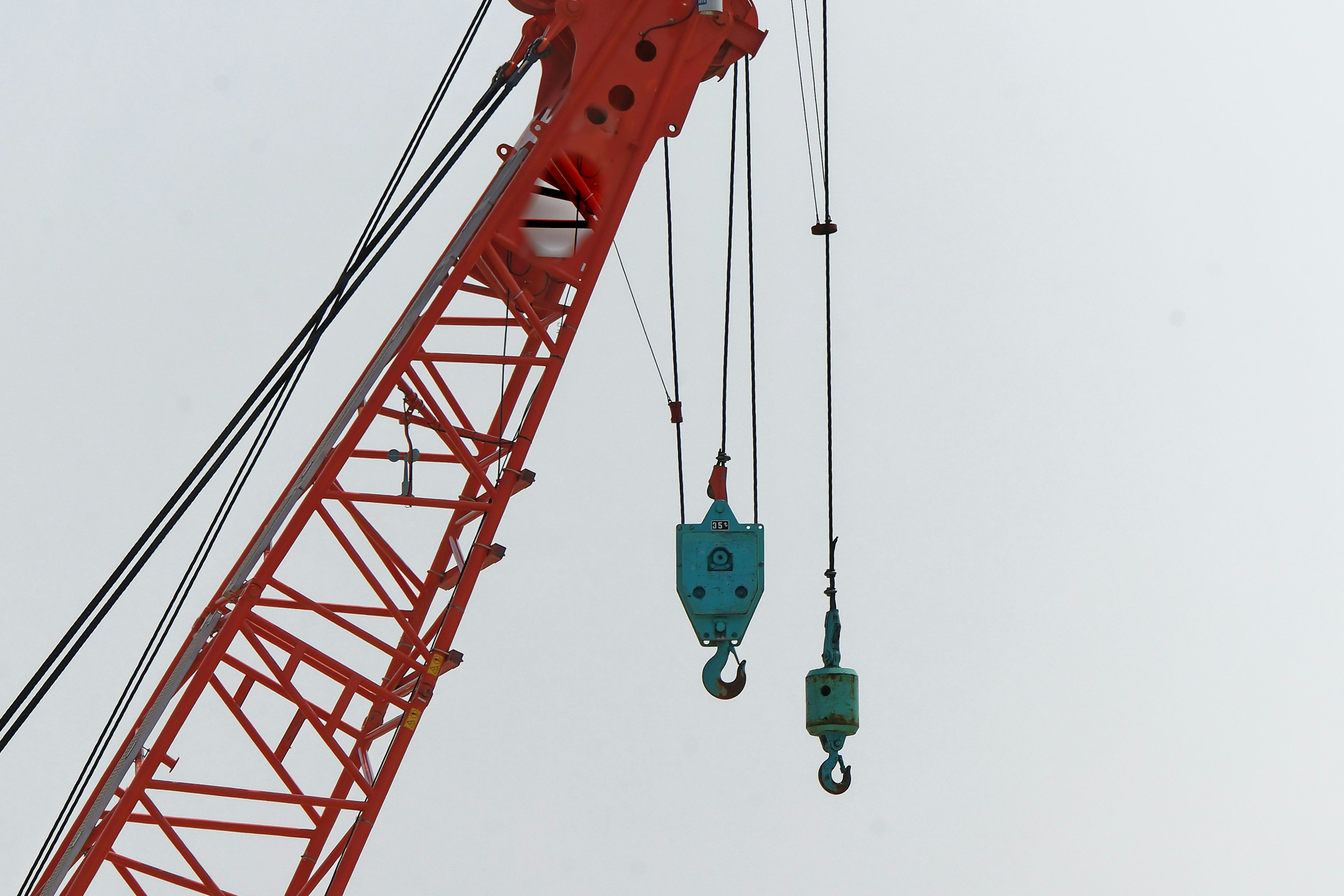 Rote Krane mit blauen Rollen und Haken, die gegen einen grauen Himmel hängen