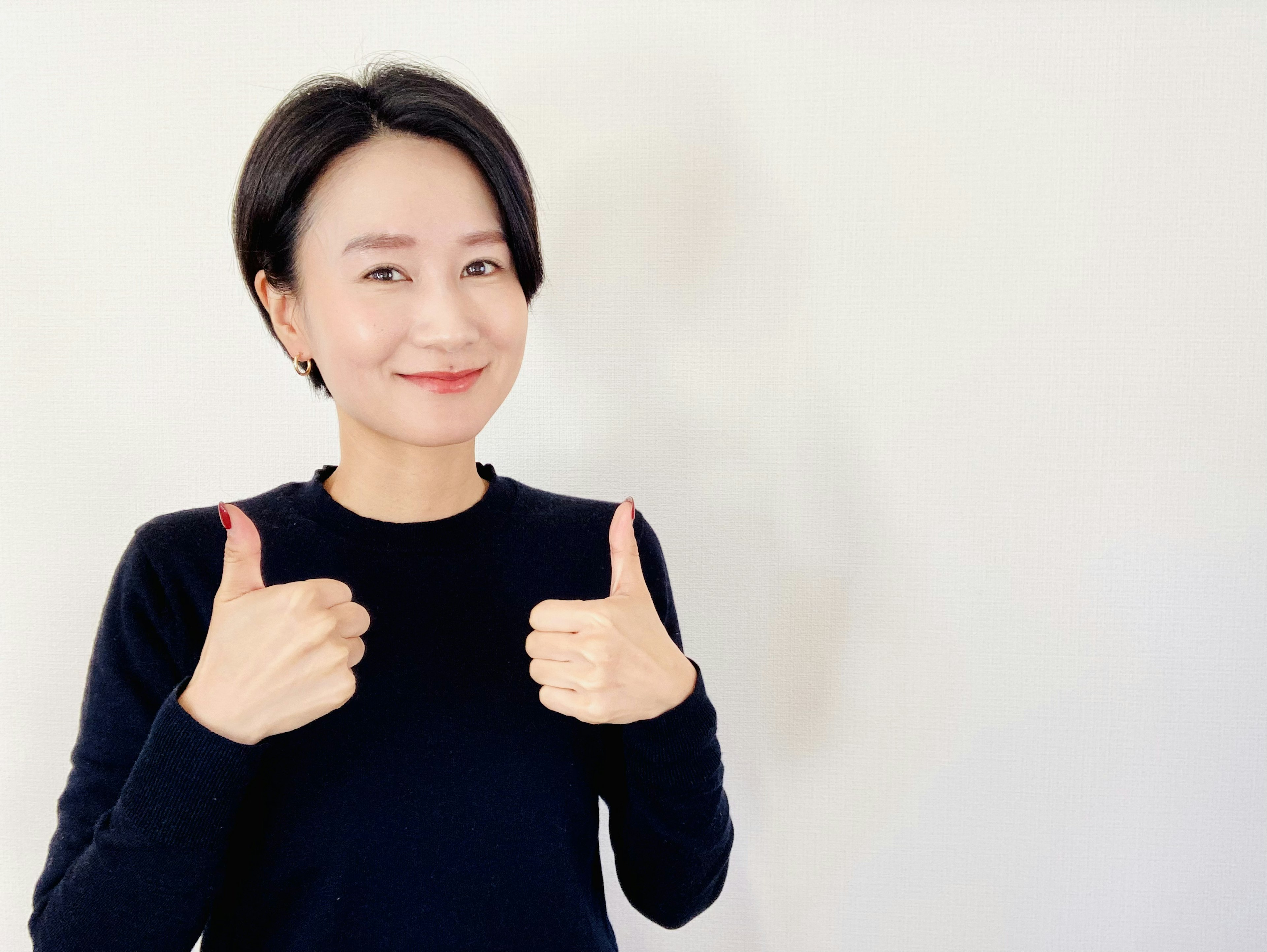 A woman smiling and giving a thumbs up in a simple portrait