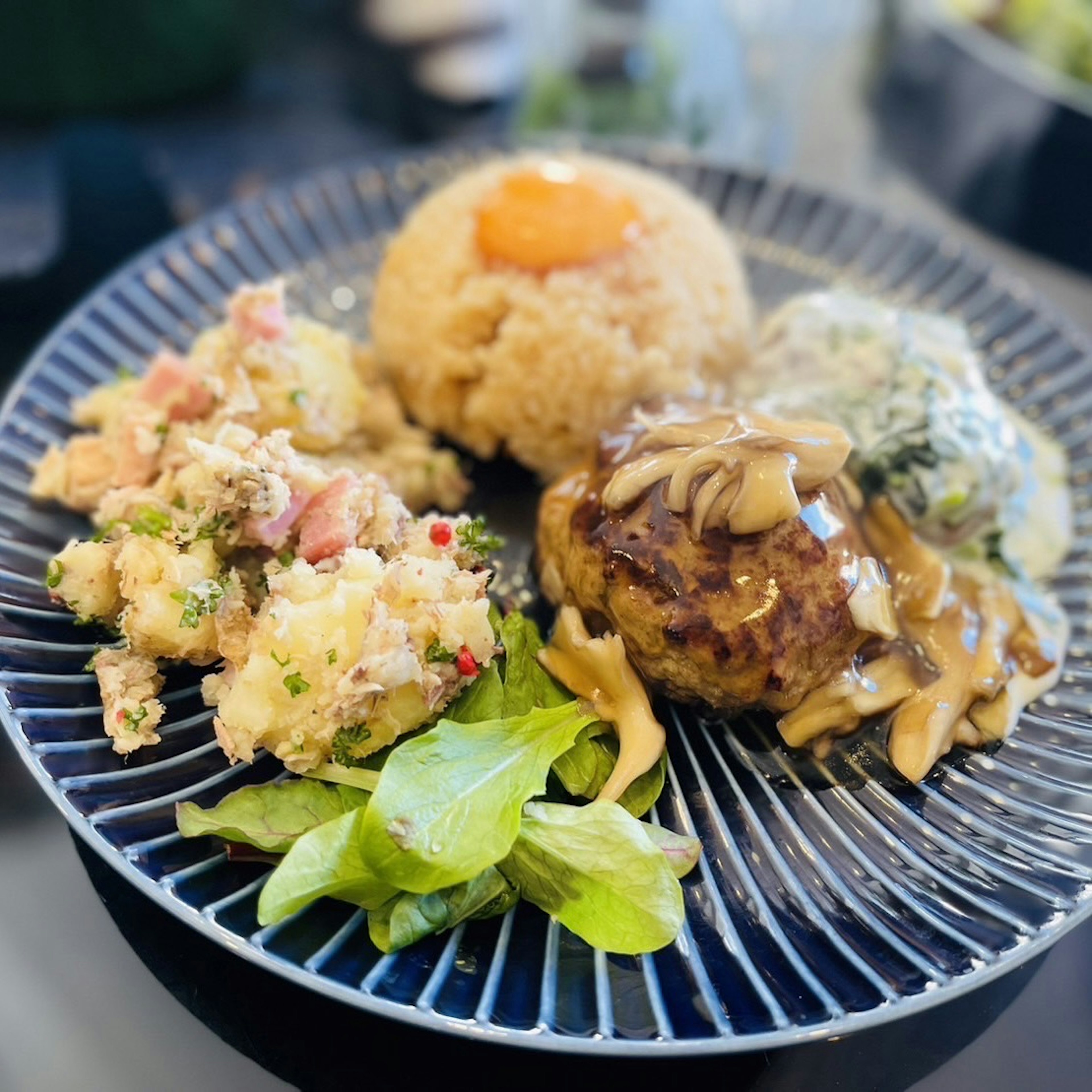 Une assiette avec des plats colorés comprenant un steak haché du riz une salade et une salade de macaronis