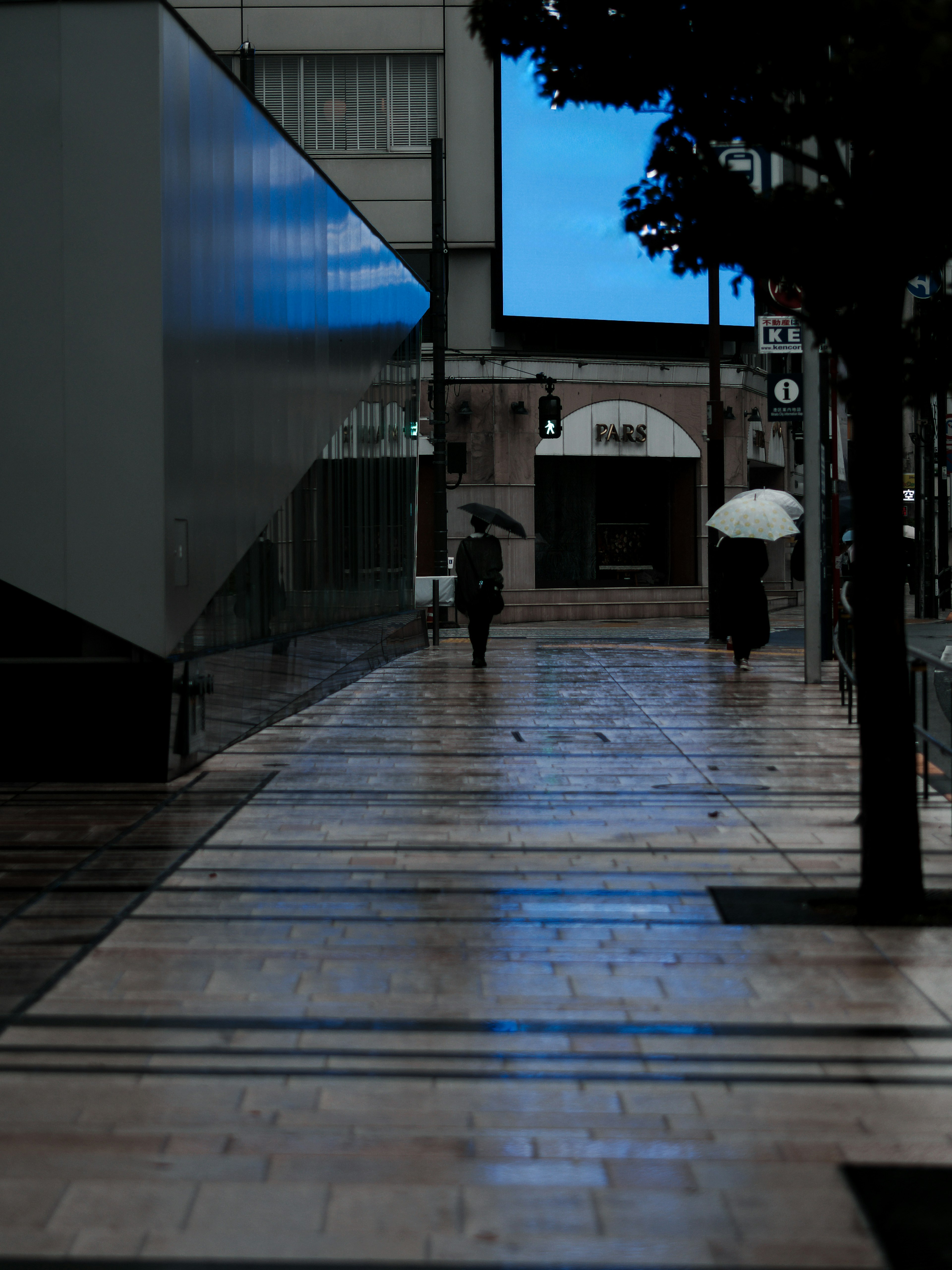 Eine Person, die im Regen auf einer Stadtstraße mit Regenschirmen geht