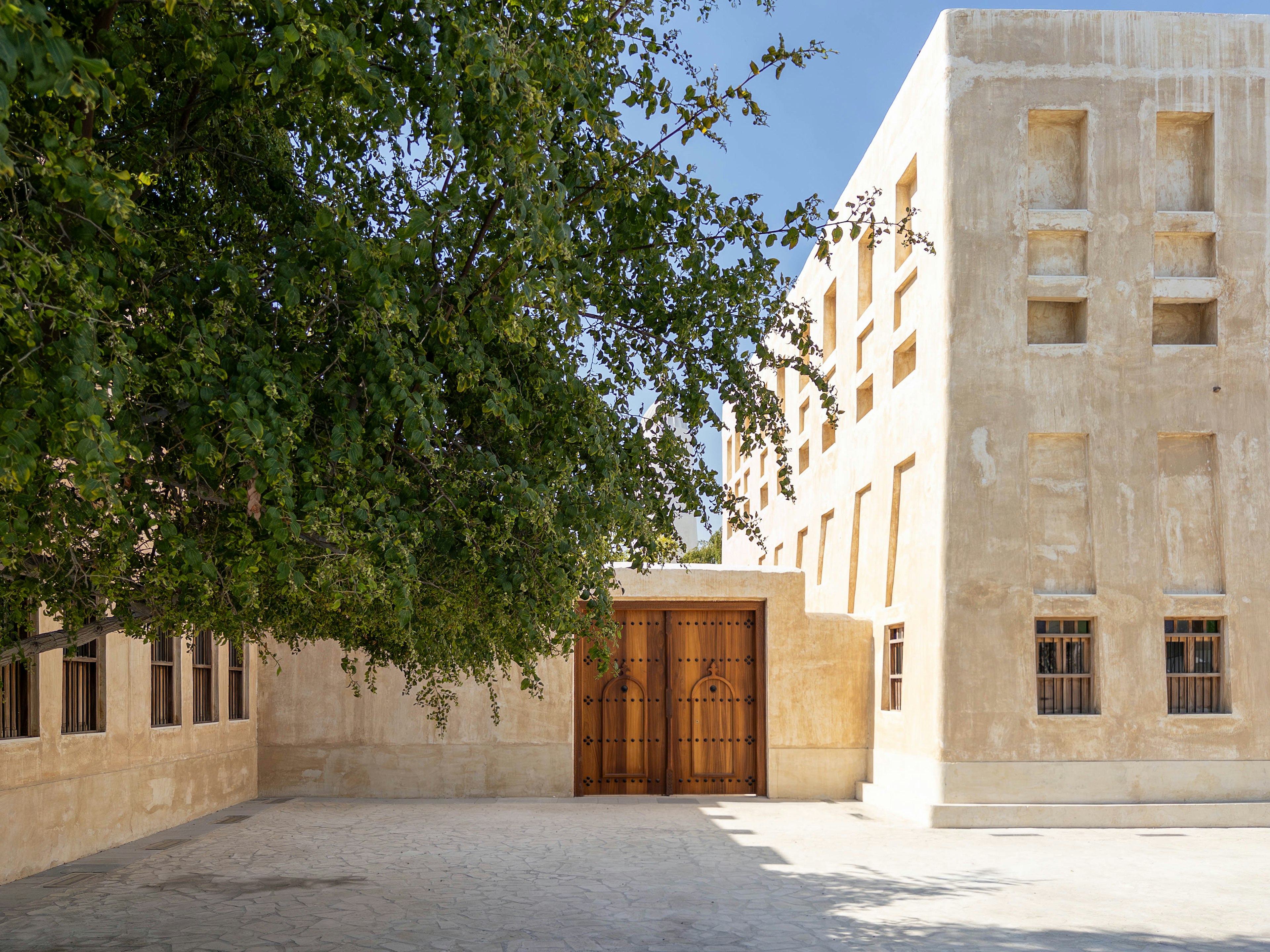 Bâtiment lumineux avec portes en bois dans une cour sous un ciel bleu