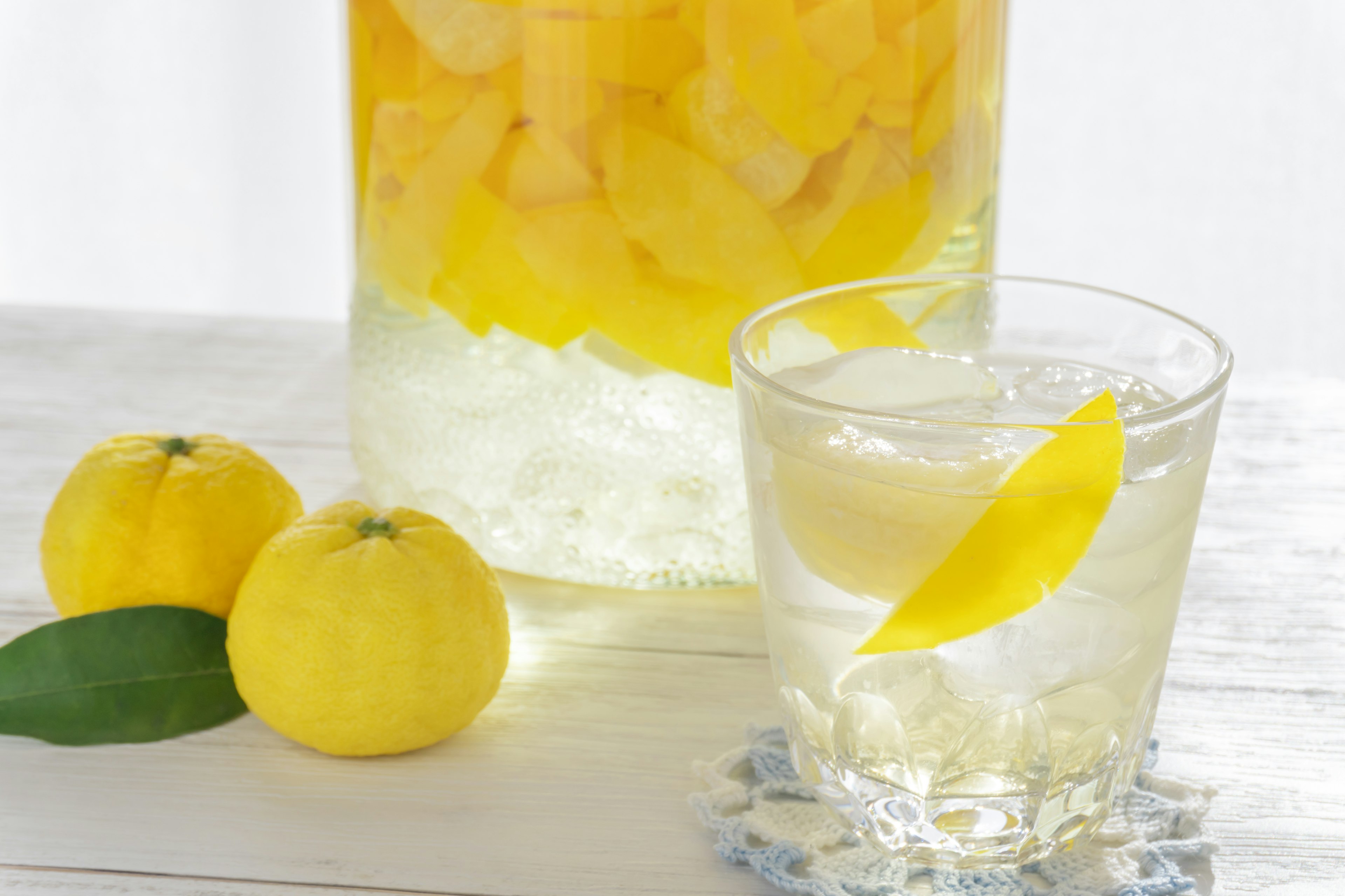 Ein Glas mit schwimmenden Zitronenscheiben in einem Getränk neben gelben Früchten und einem Krug mit infundierter Flüssigkeit