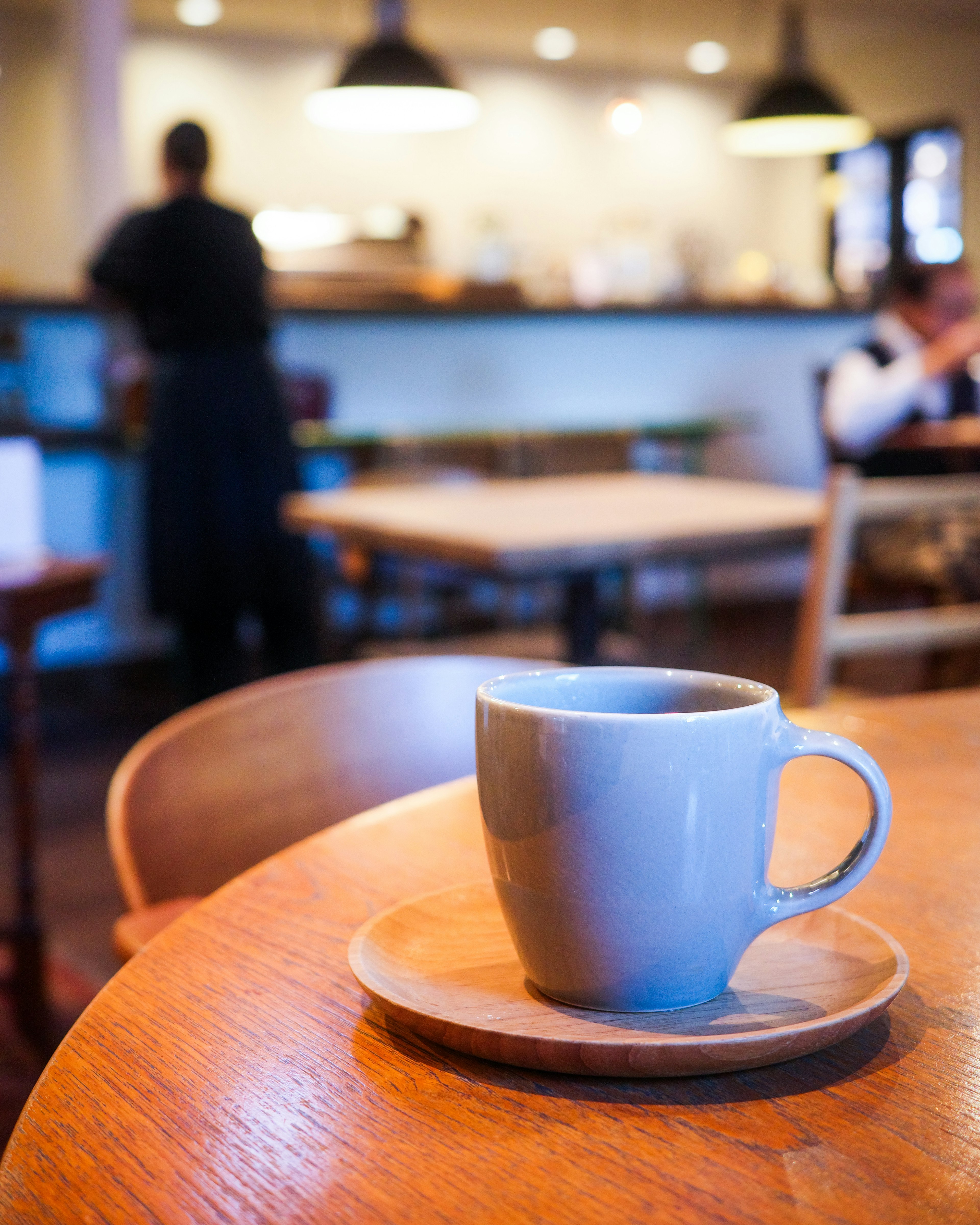 Una tazza di caffè blu su un tavolo di legno in un caffè con un membro dello staff e clienti sullo sfondo