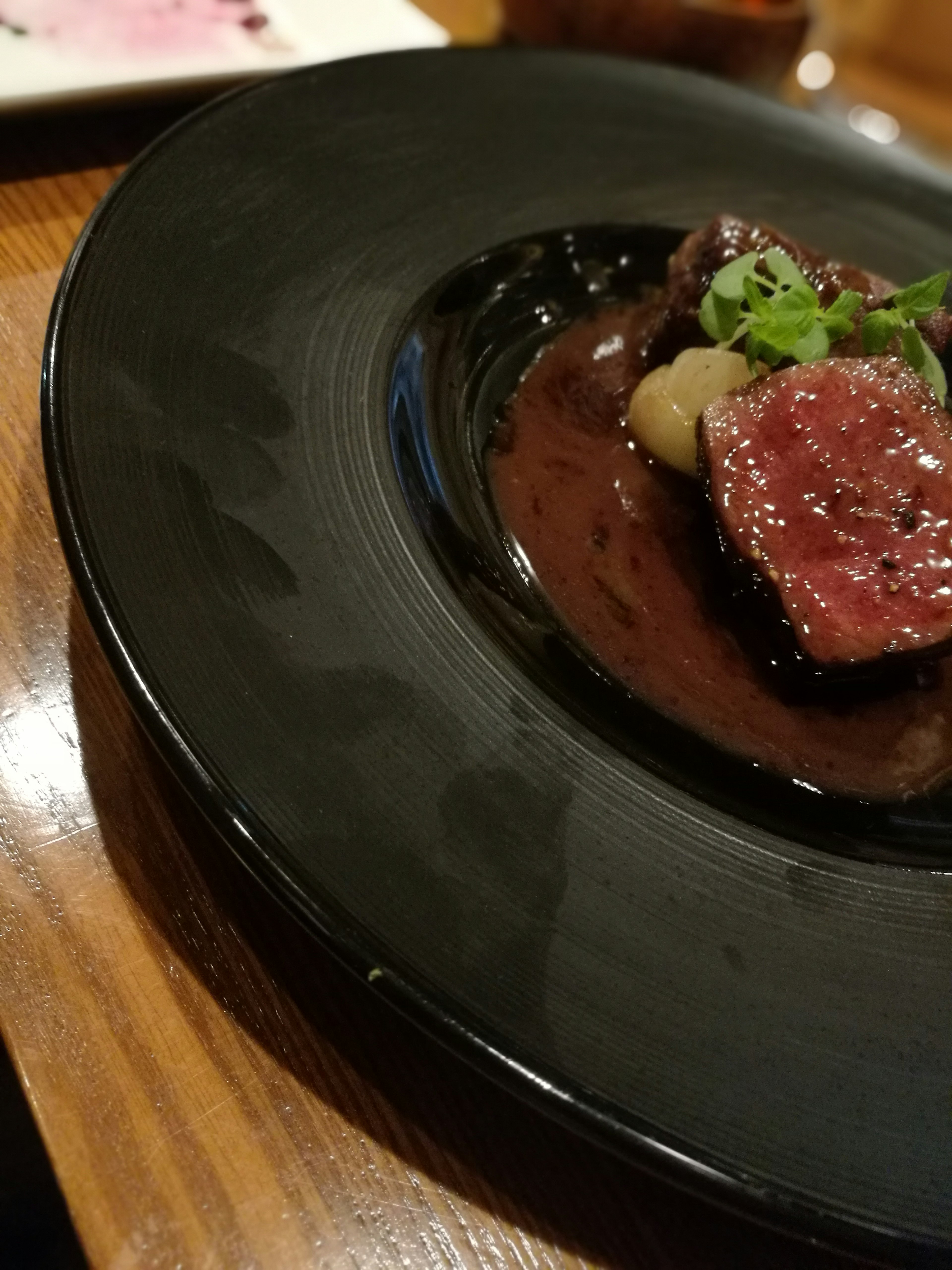 A gourmet dish featuring steak on a black plate with sauce and garnishes